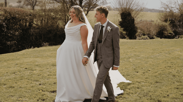 Bride and groom walking hand in hand through a scenic field during their wedding at Priston Mill.