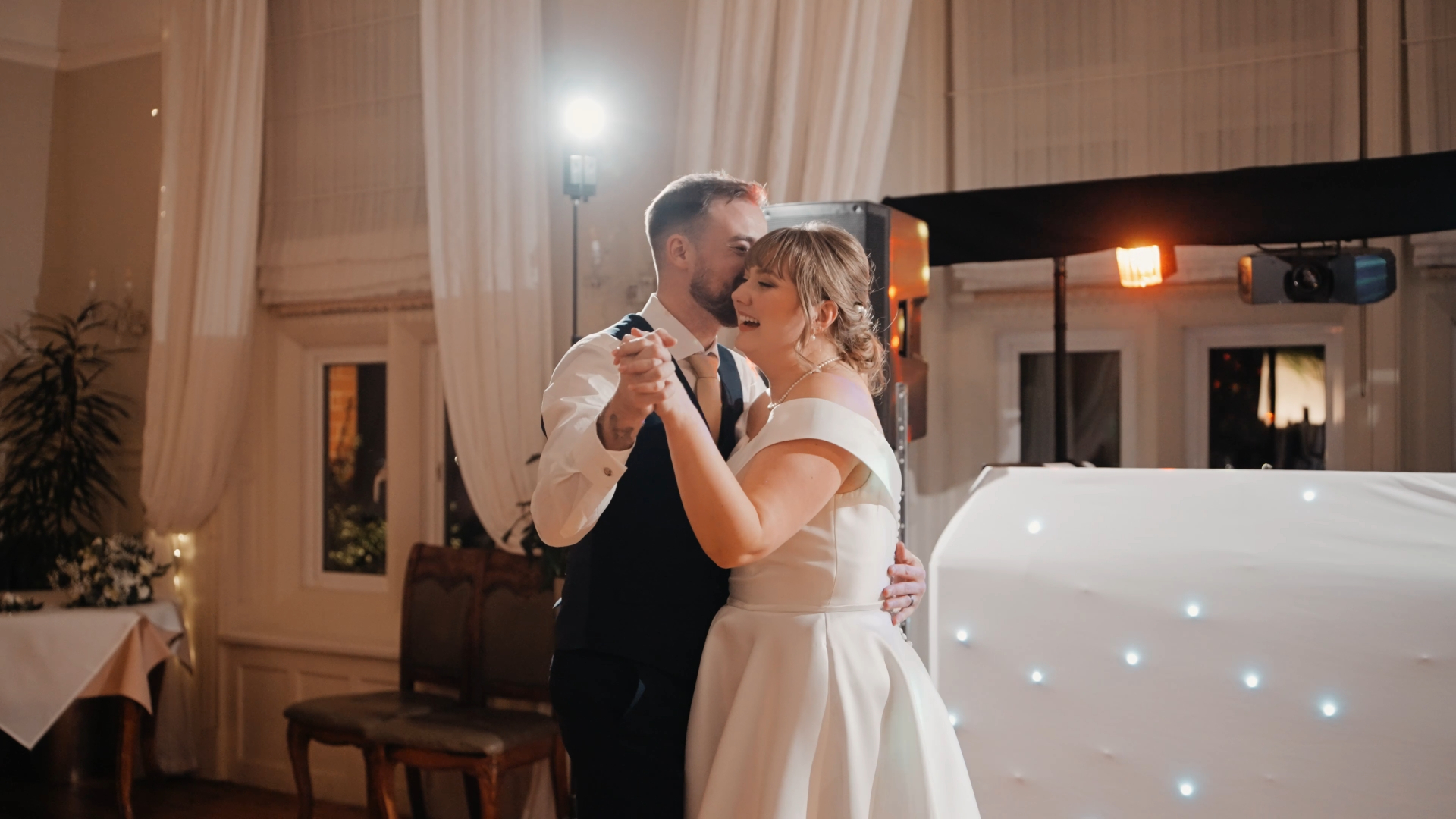 A bride and groom share a romantic first dance at their intimate wedding at Berwick Lodge, holding each other closely and smiling, with soft lighting and elegant decor in the background.