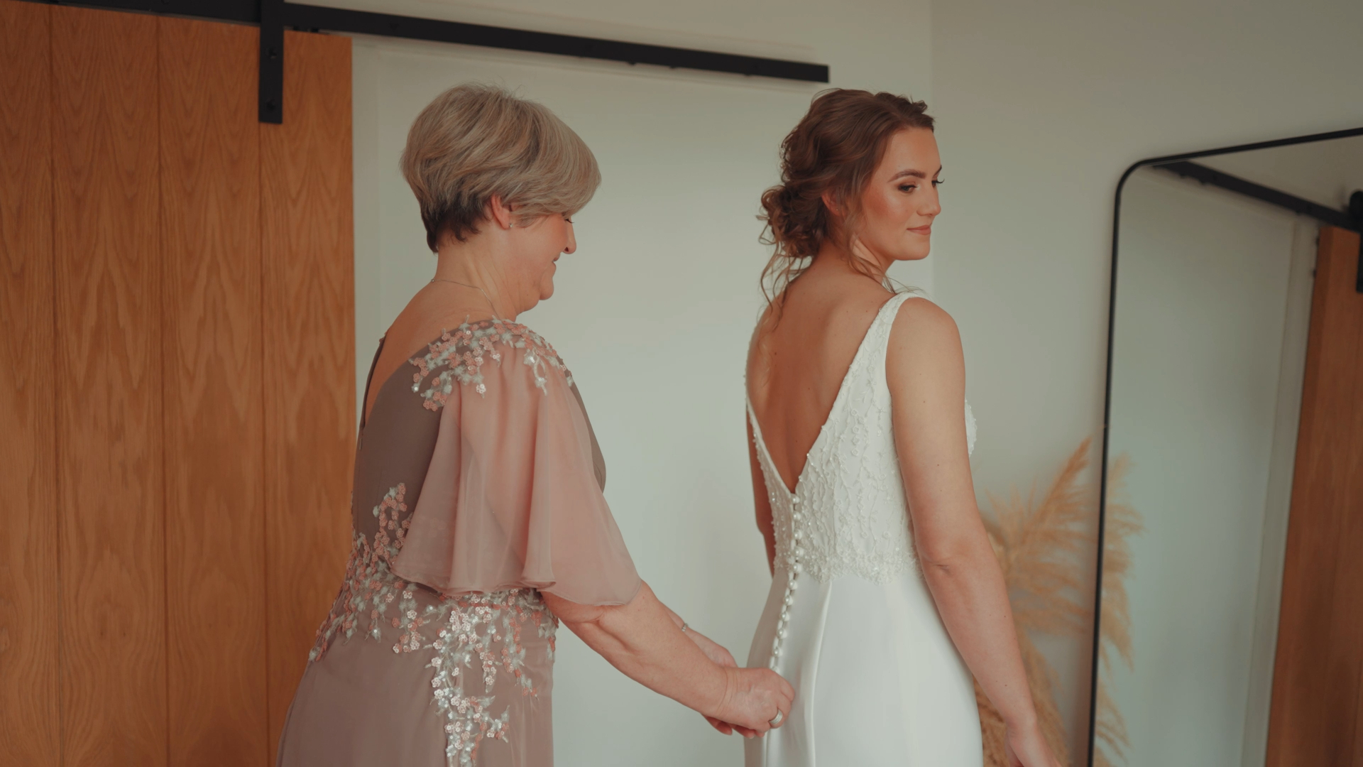 Bride looking to the side as her mother zips up her dress — an emotional, behind-the-scenes moment captured by a documentary wedding videographer.