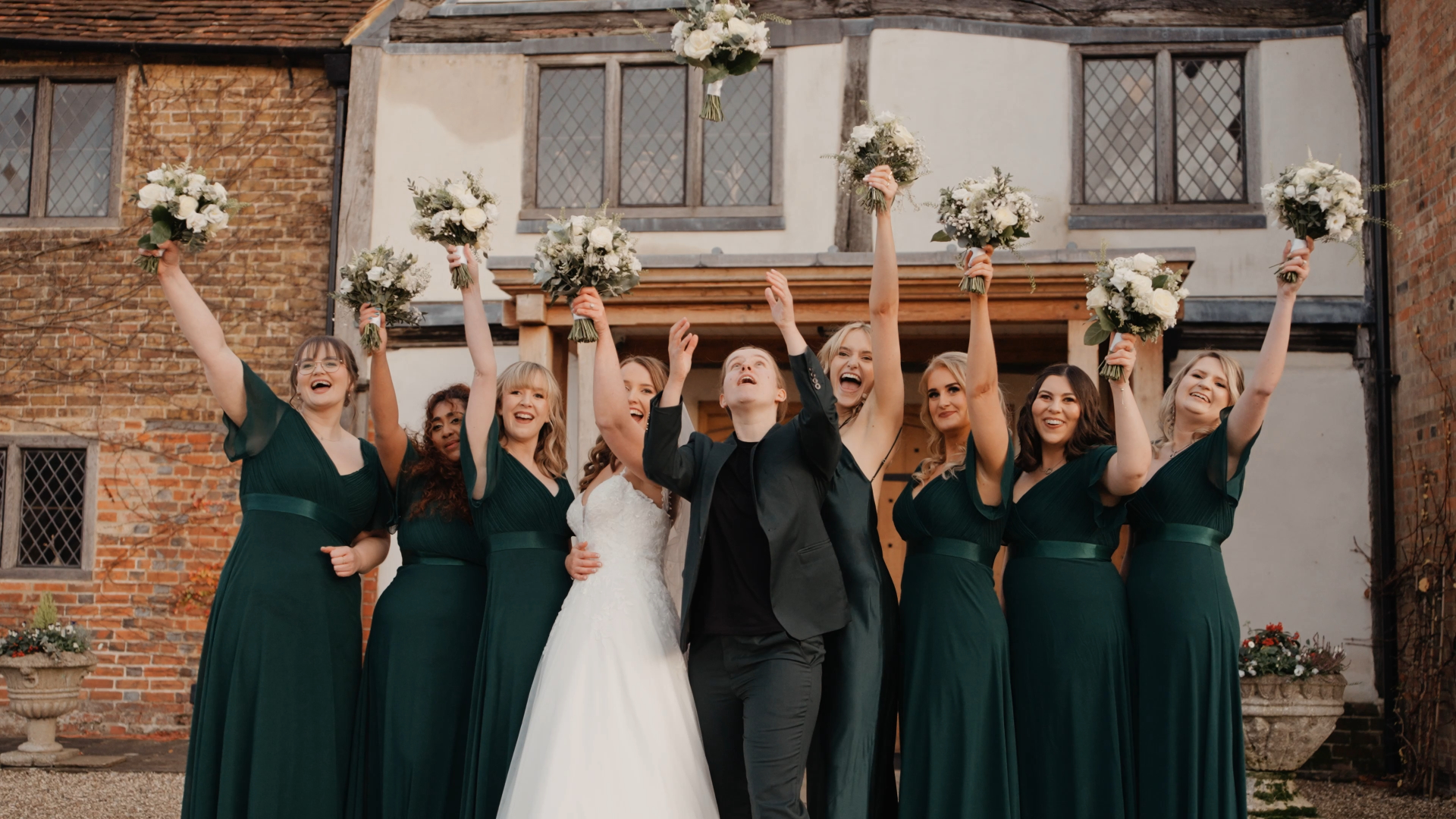 Bride, groom, and bridal party joyfully tossing flowers in the air, a fun candid moment documented by a documentary wedding videographer.