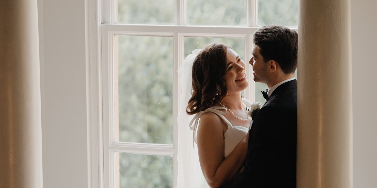 Candid moment during a wedding at Crowcombe Court with the groom leaning on a wall and the bride laughing beside him.

