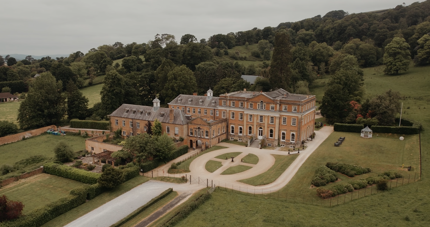 Aerial view of a wedding at Crowcombe Court, capturing the grand architecture and surrounding gardens from above.