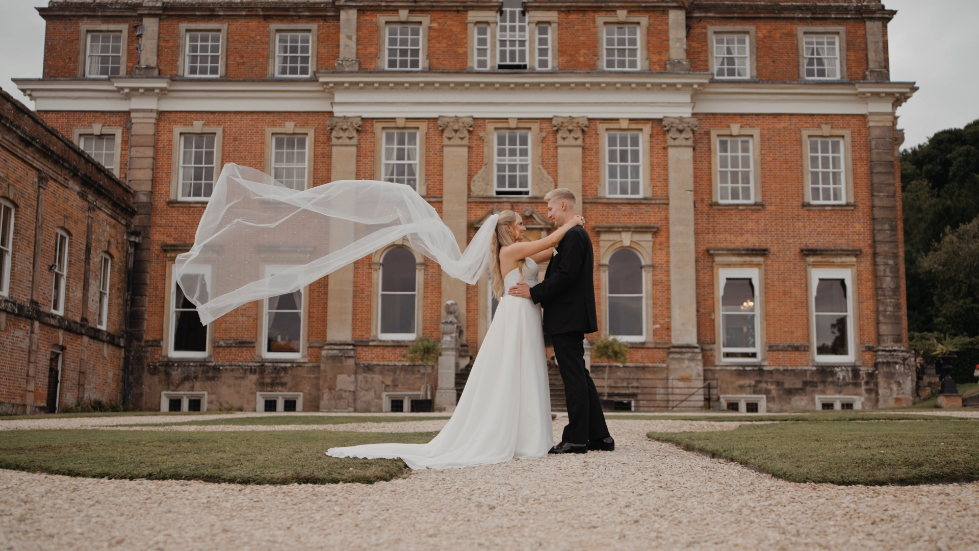 Bride and groom share an intimate wedding moment in front of Crowcombe Court, with the bride’s veil flowing in the wind as they embrace and gaze lovingly into each other’s eyes.