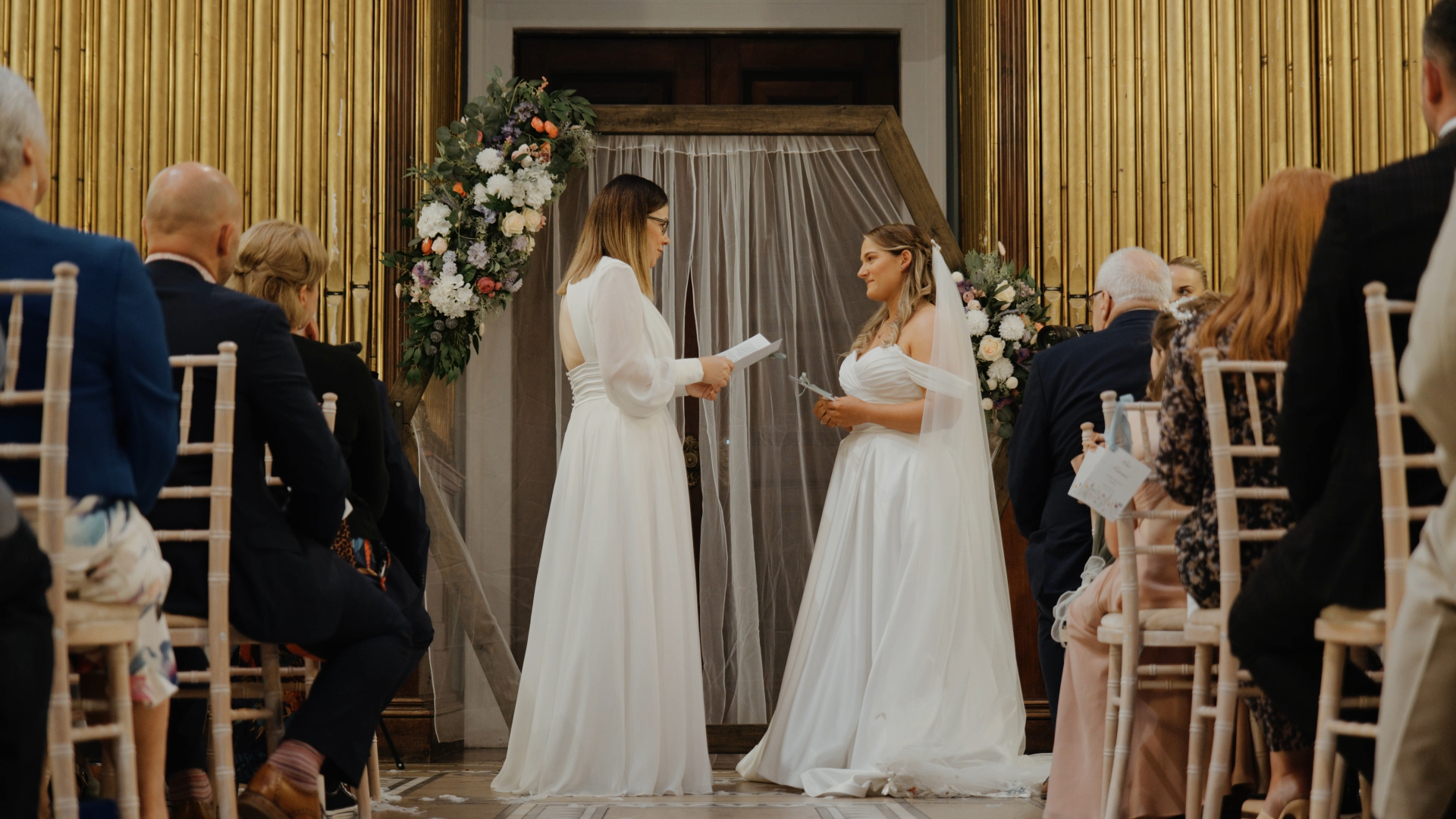 Two brides exchanging vows in front of their loved ones, surrounded by love and heartfelt emotion.