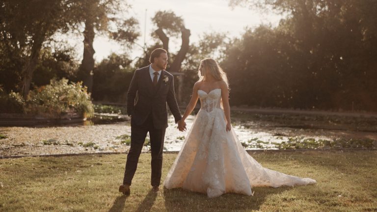 Bride and groom walking hand in hand through the gardens of Clevedon Hall during golden hour