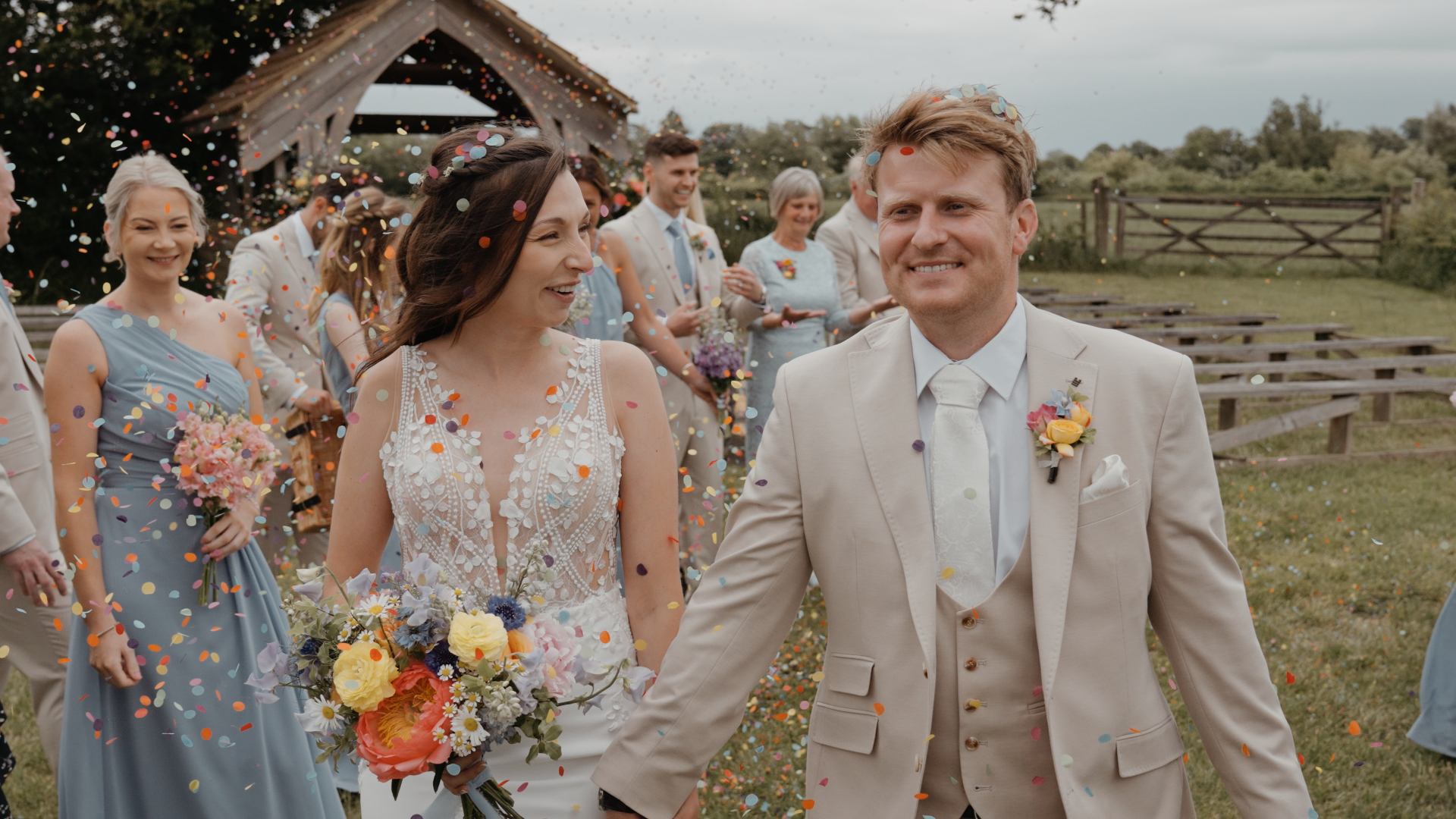 Newlyweds walk down the aisle as guests toss vibrant confetti with joyful, celebratory reactions during a Somerset wedding ceremony.