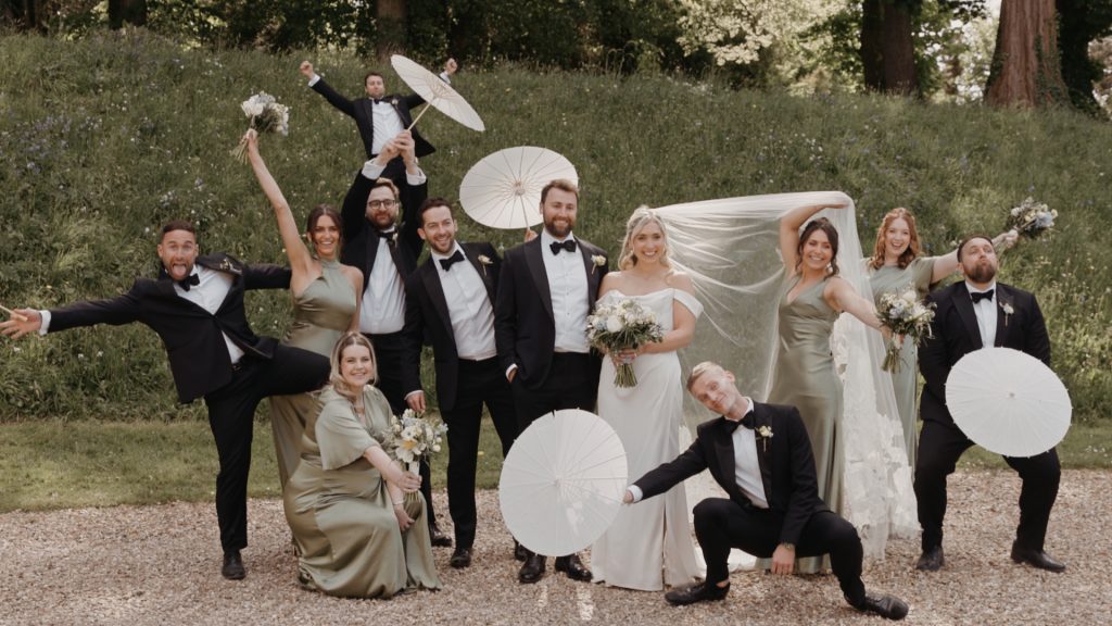 Bride and groom strike silly poses with fun props alongside their bridesmaids and groomsmen at Coombe Lodge in Somerset, all laughing and looking joyfully happy.