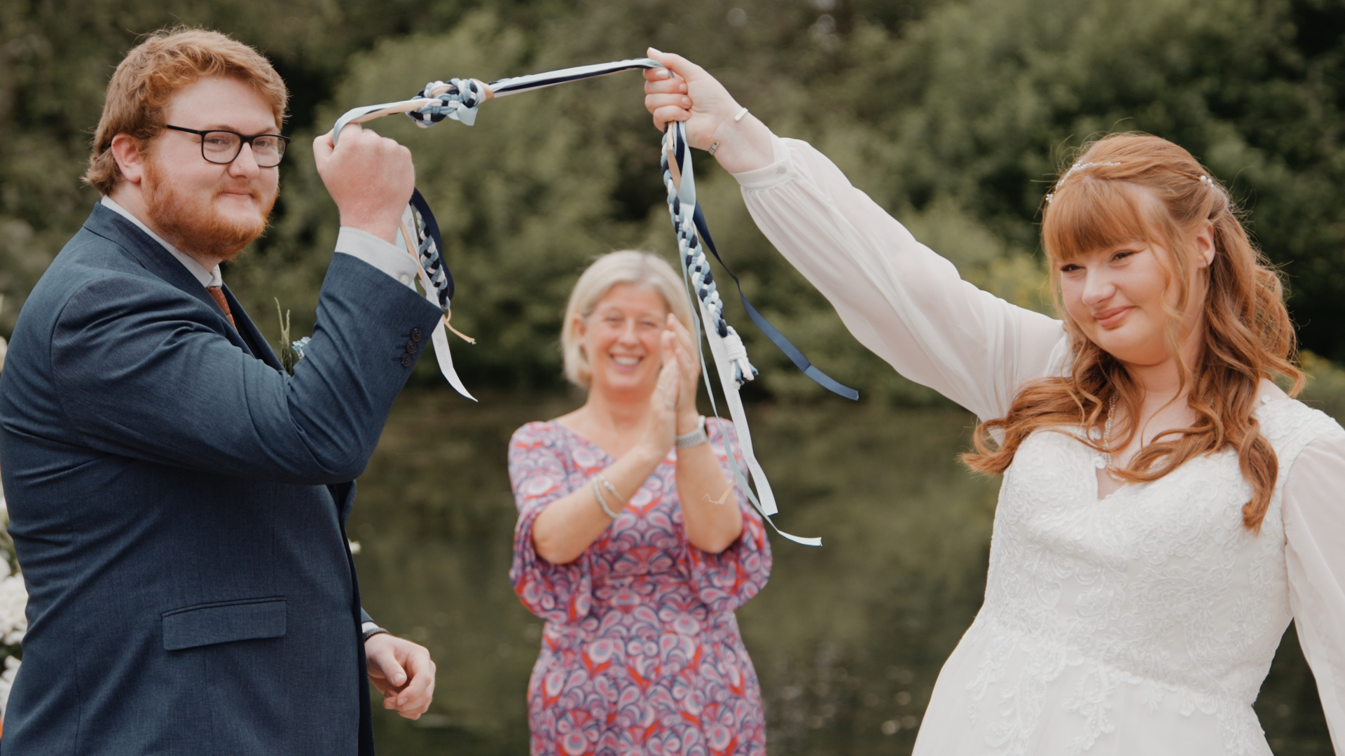 Bride and groom raising their tied ribbons during a joyful handfasting ceremony at Hornsbury Mill.