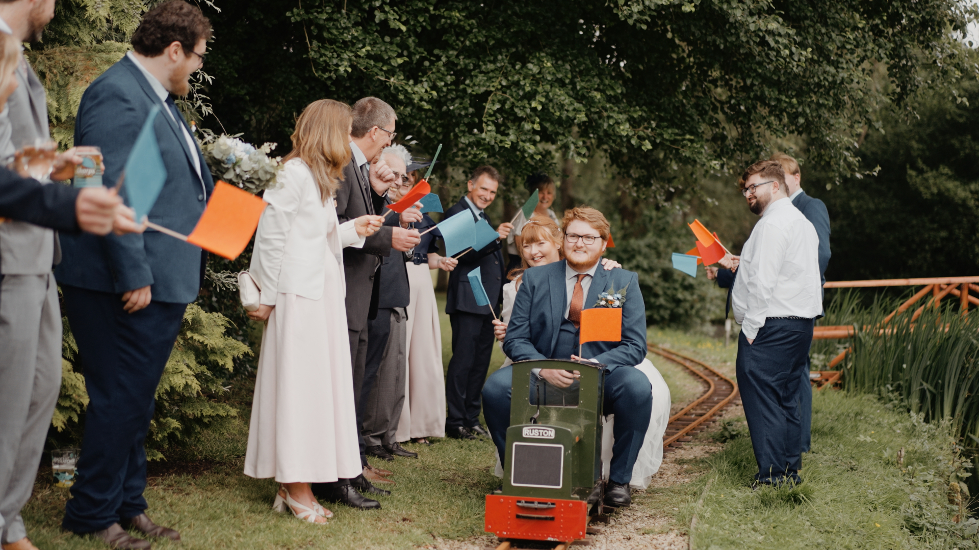 Bride and groom riding a miniature train surrounded by cheering guests at Hornsbury Mill during their summer wedding.