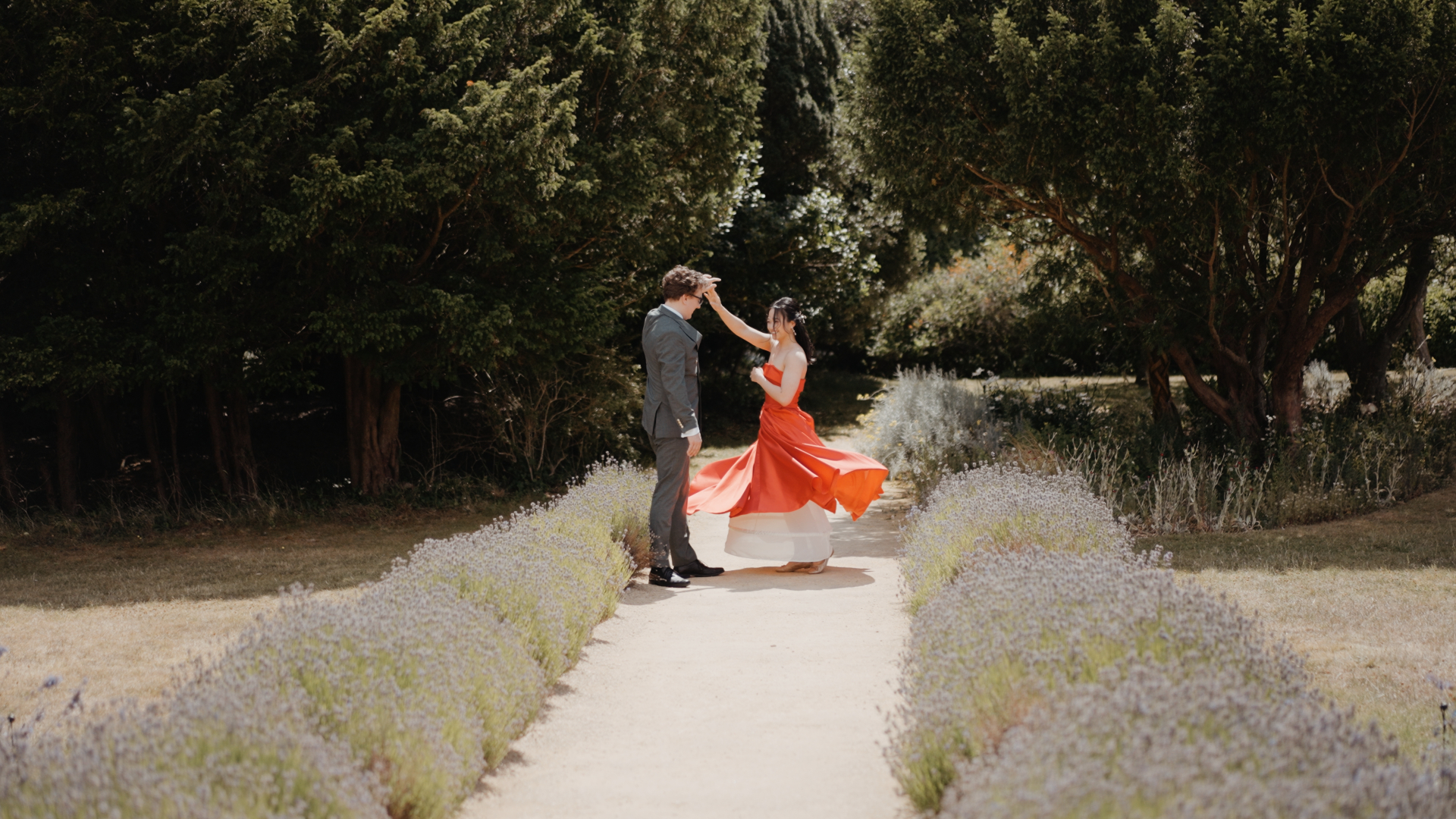 Bride twirling in a red dress with the groom along the lavender path at Clevedon Hall gardens.