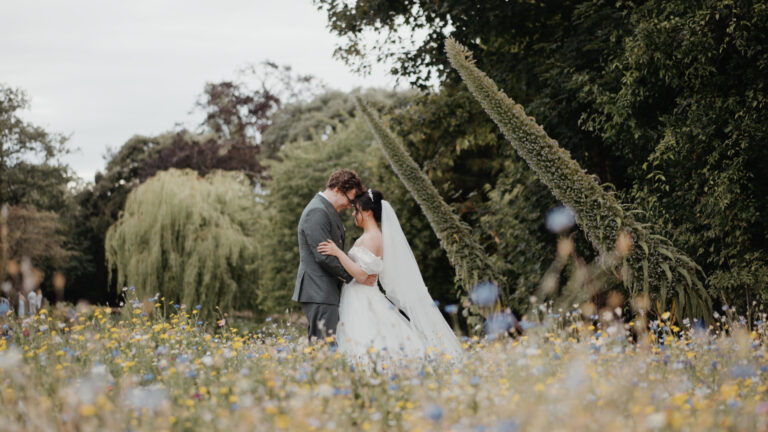 Bride and groom sharing an intimate embrace in a wildflower meadow during a summer wedding at Clevedon Hall, Somerset.
