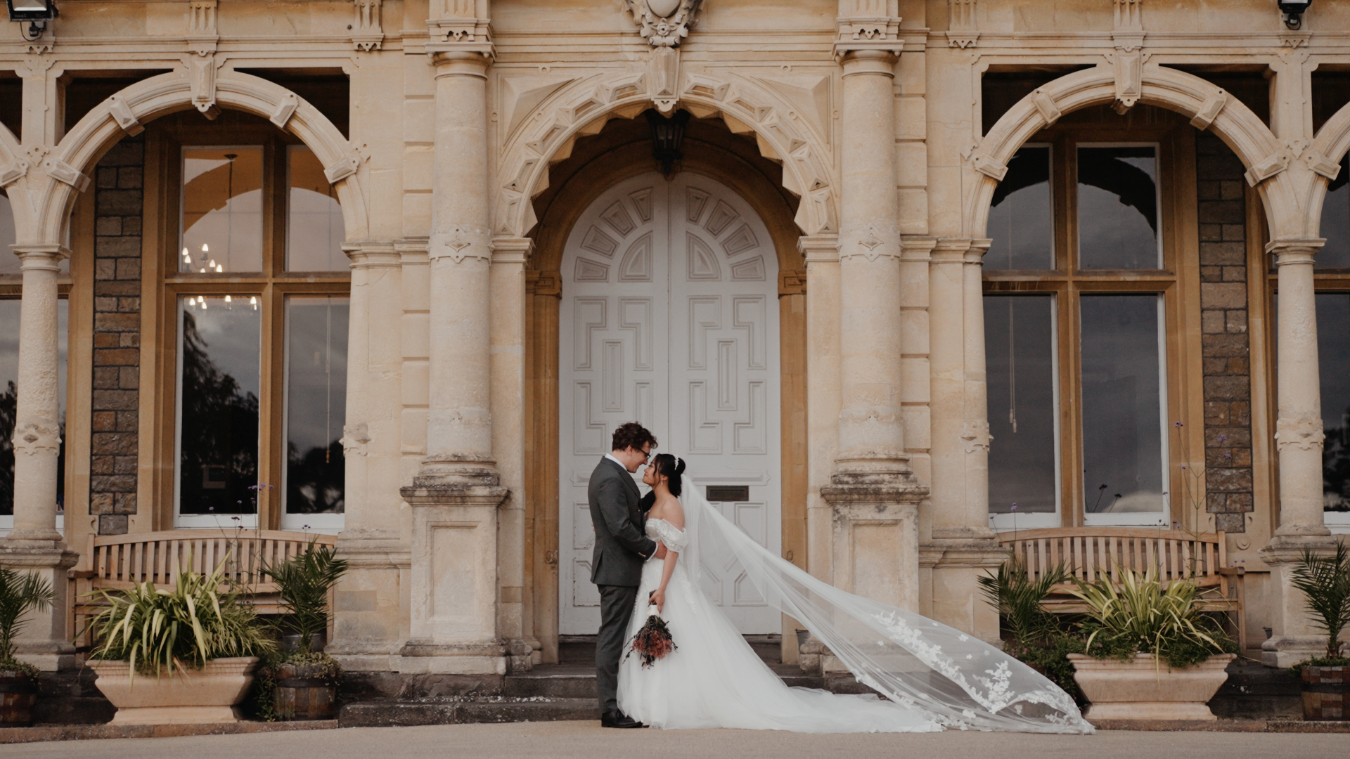 Newlyweds embracing in front of the grand stone archway at Clevedon Hall.