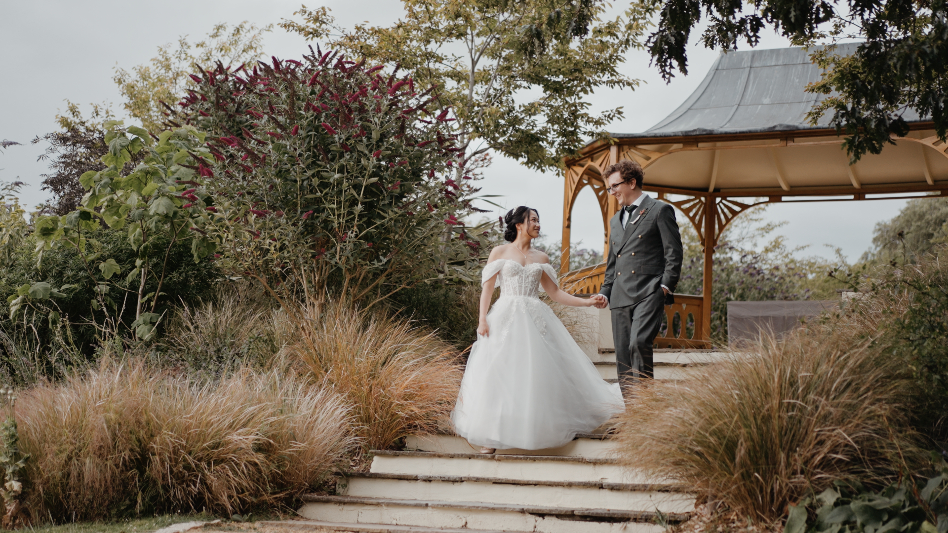 Bride and groom holding hands and walking down the garden steps near the gazebo at Clevedon Hall.