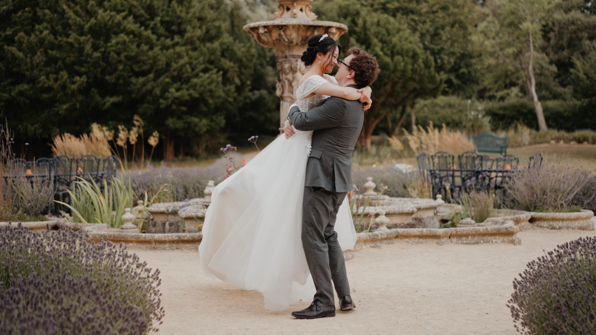 Groom lifting the bride in his arms for a joyful moment by the fountain at a Somerset wedding.