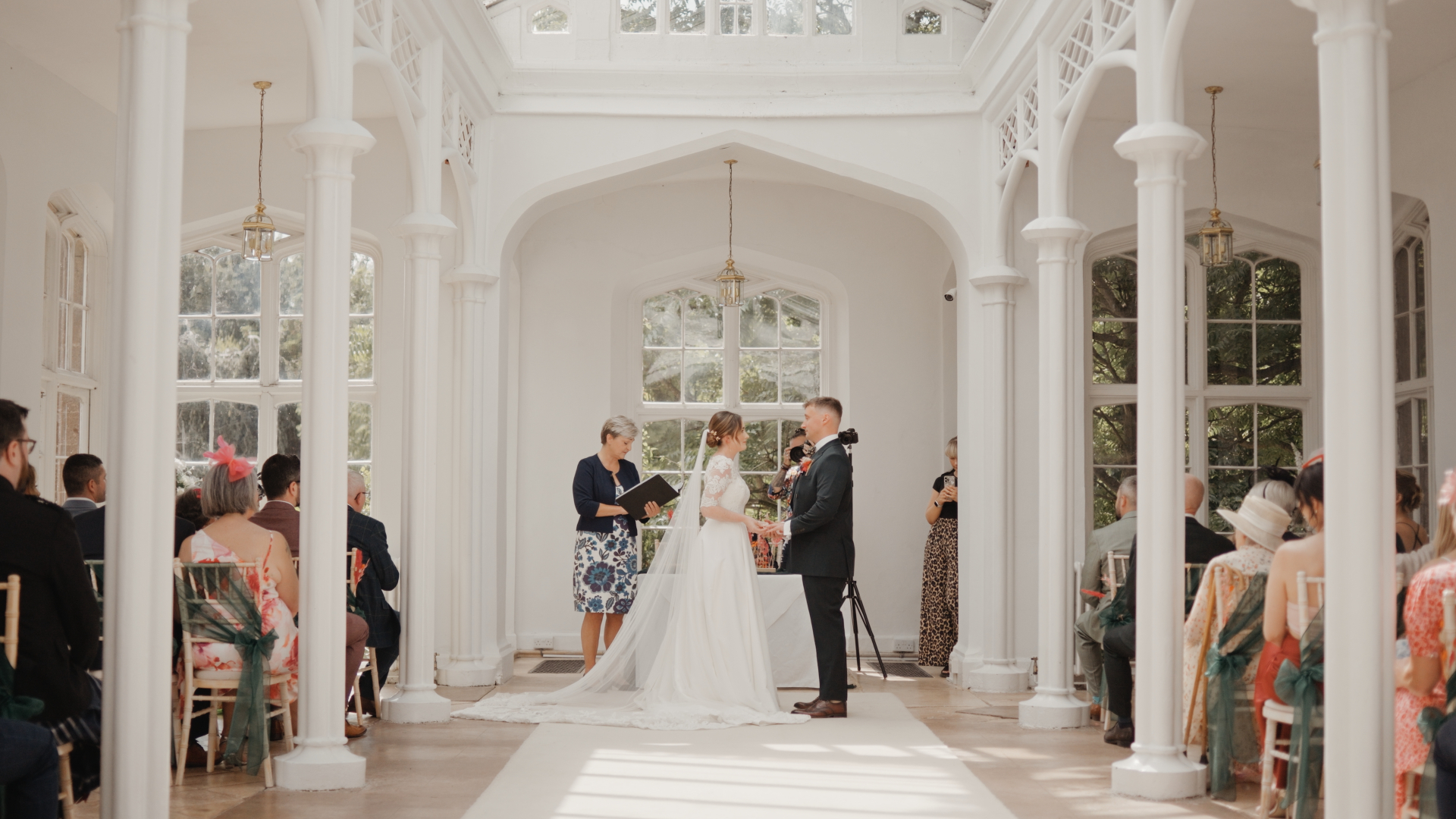 The bride and groom exchange vows inside the bright orangery at St Audries Park during their Somerset wedding ceremony.