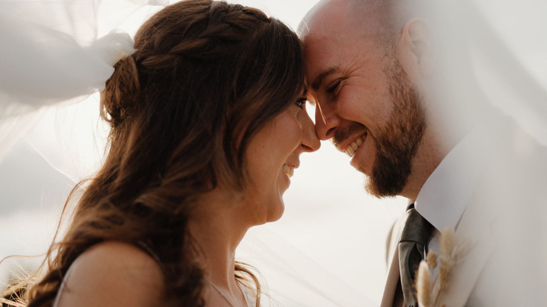 Close-up of the bride and groom under the veil, smiling softly with sunlight glowing through the fabric — a tender rustic wedding moment at Humber Barn.