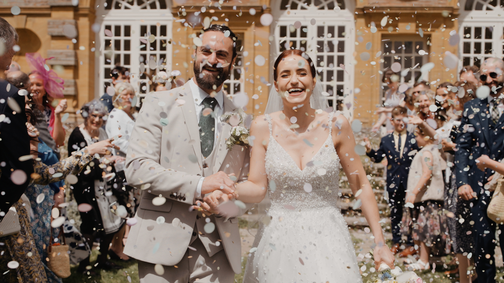 The newlyweds walk through a shower of confetti, smiling and laughing. This joyful moment is a highlight of wedding videography.