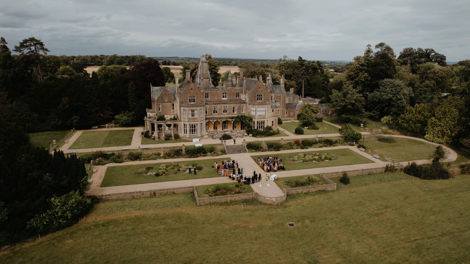 Drone footage of Orchardleigh House in Somerset, revealing its grand gardens and ceremony setup framed by lush greenery.