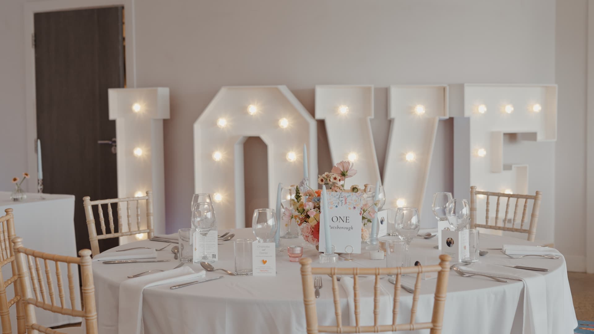 Elegant wedding reception setup with large illuminated LOVE letters and pastel flowers creating a romantic atmosphere.