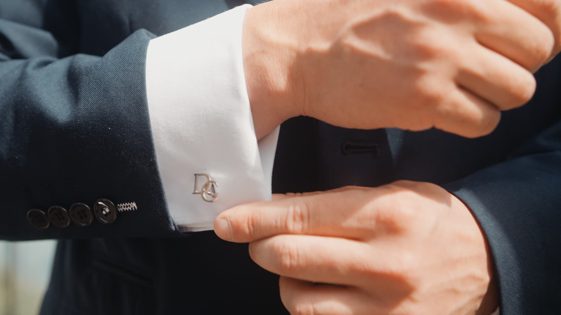 Close-up of groom fastening cufflinks engraved with initials, captured by a wedding videographer in Devon.