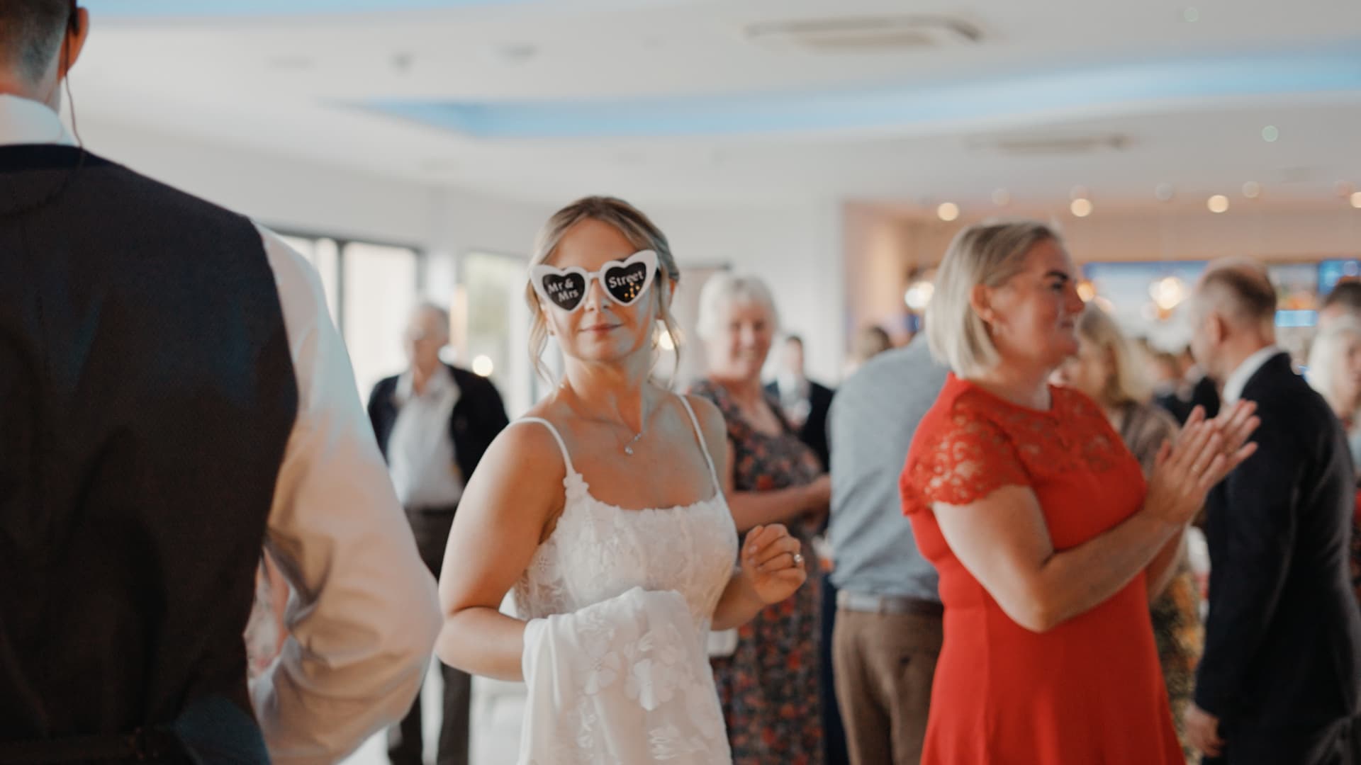 Bride dancing with friends wearing personalised heart-shaped sunglasses during the evening celebration.
