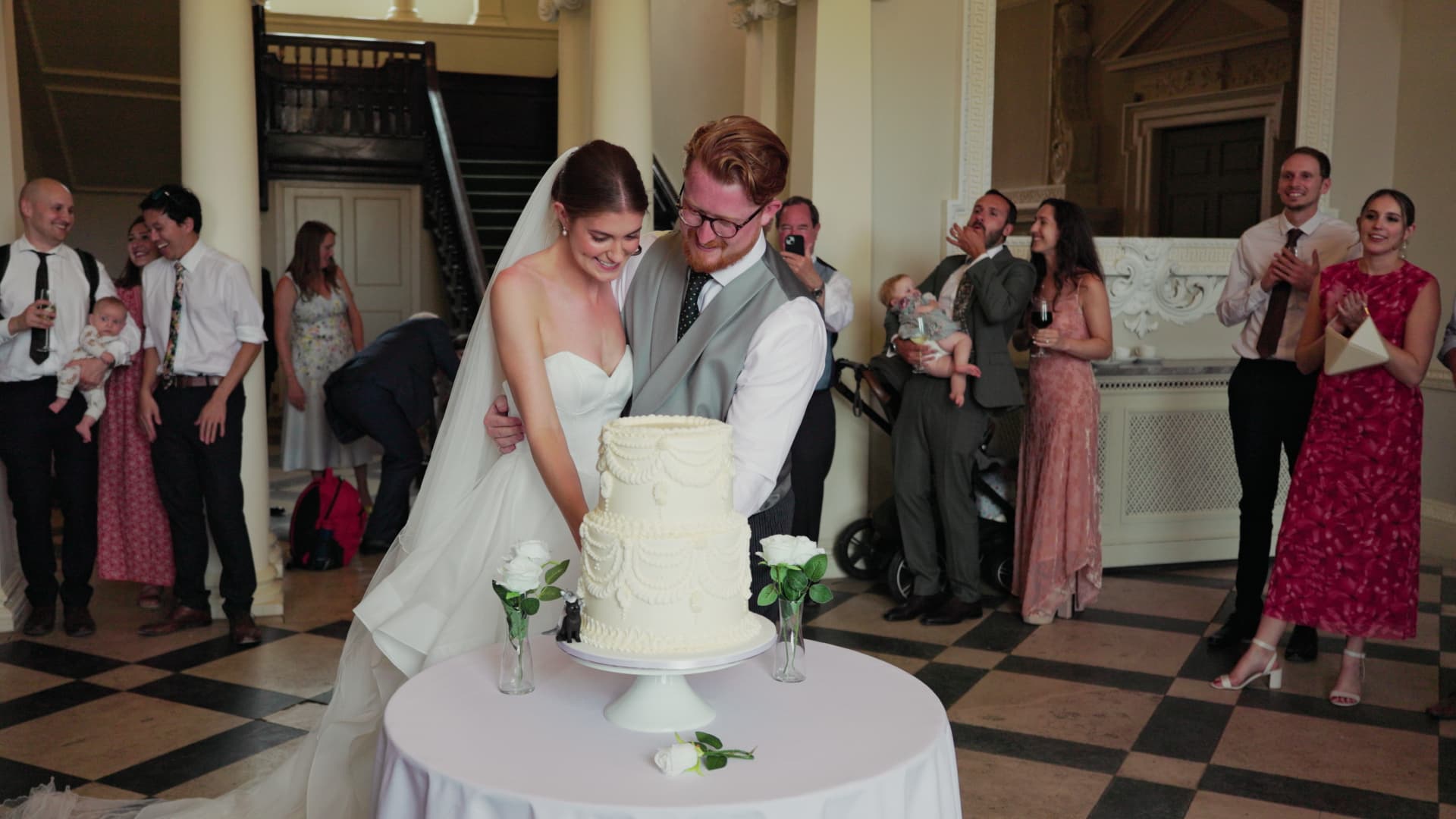 Bride and groom cutting their elegant white wedding cake at Crowcombe Court surrounded by smiling guests during the reception.