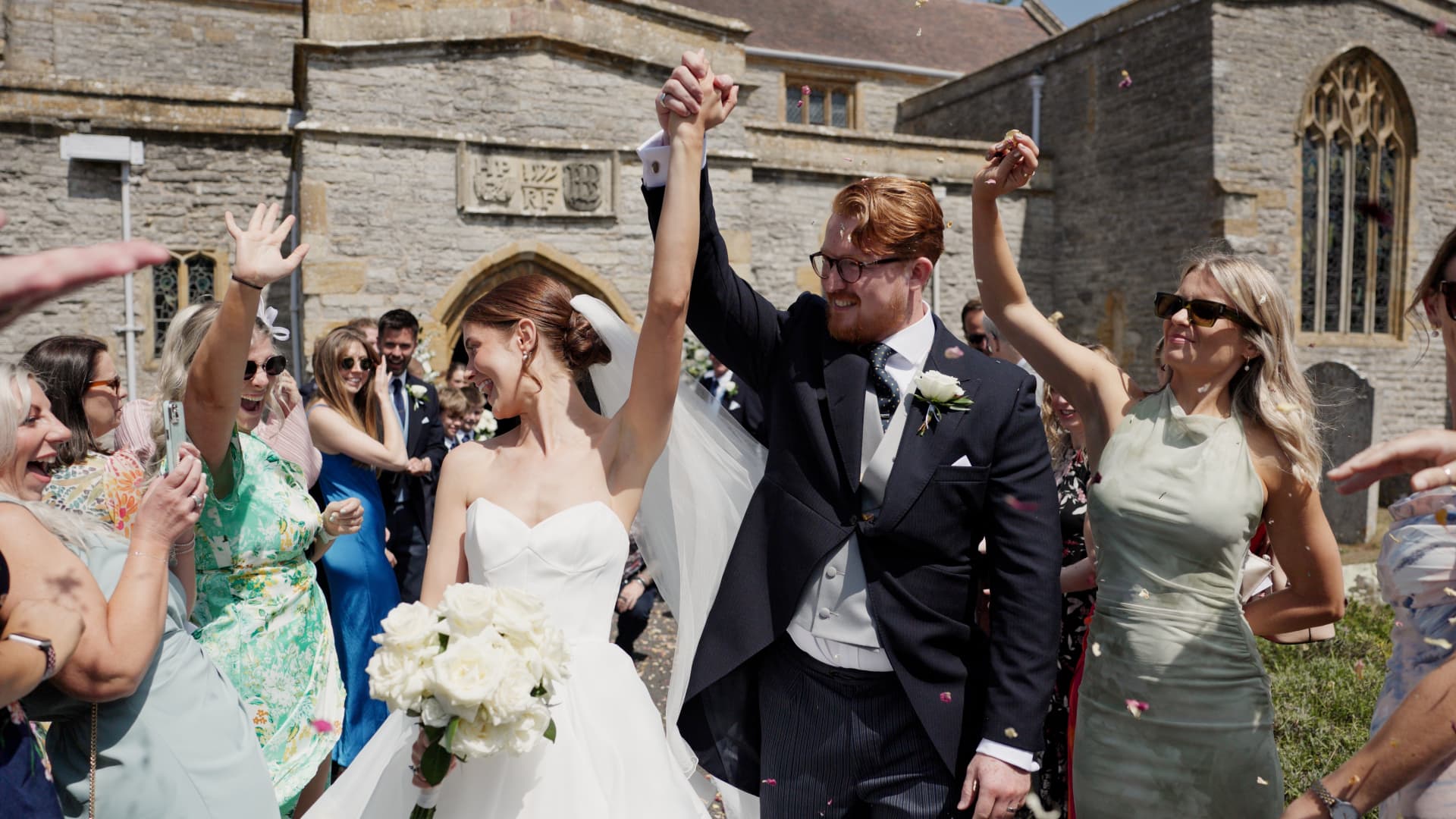 Newlyweds celebrating outside Chedzoy Church in Somerset surrounded by guests throwing confetti.