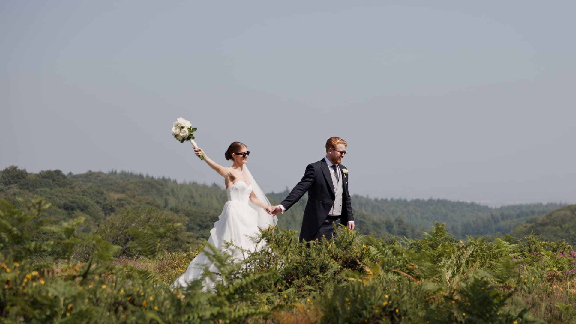 Bride and groom walking hand in hand through open fields during their outdoor wedding portraits.