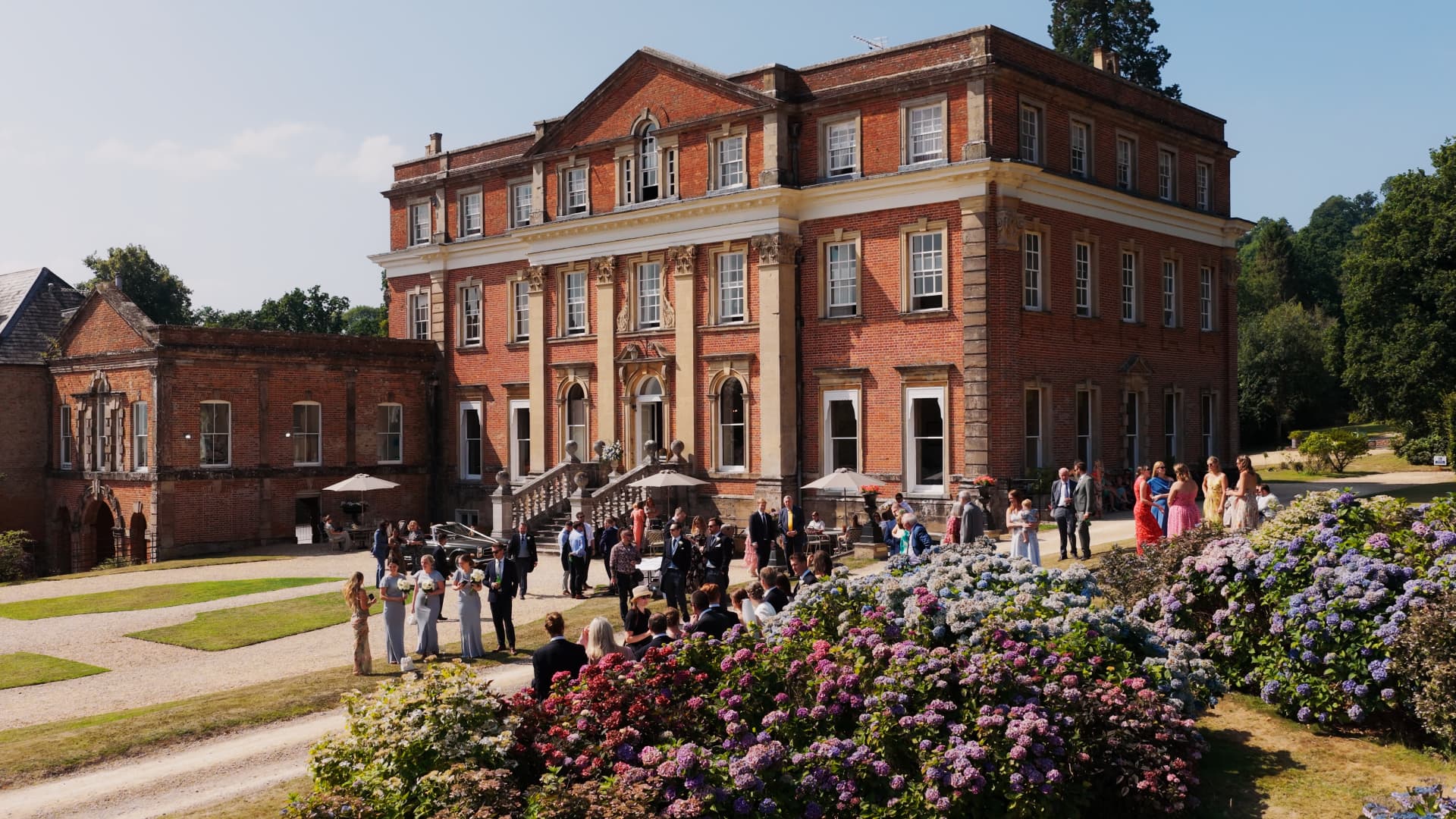 A stunning view of Crowcombe Court with guests mingling outside during a summer wedding celebration.