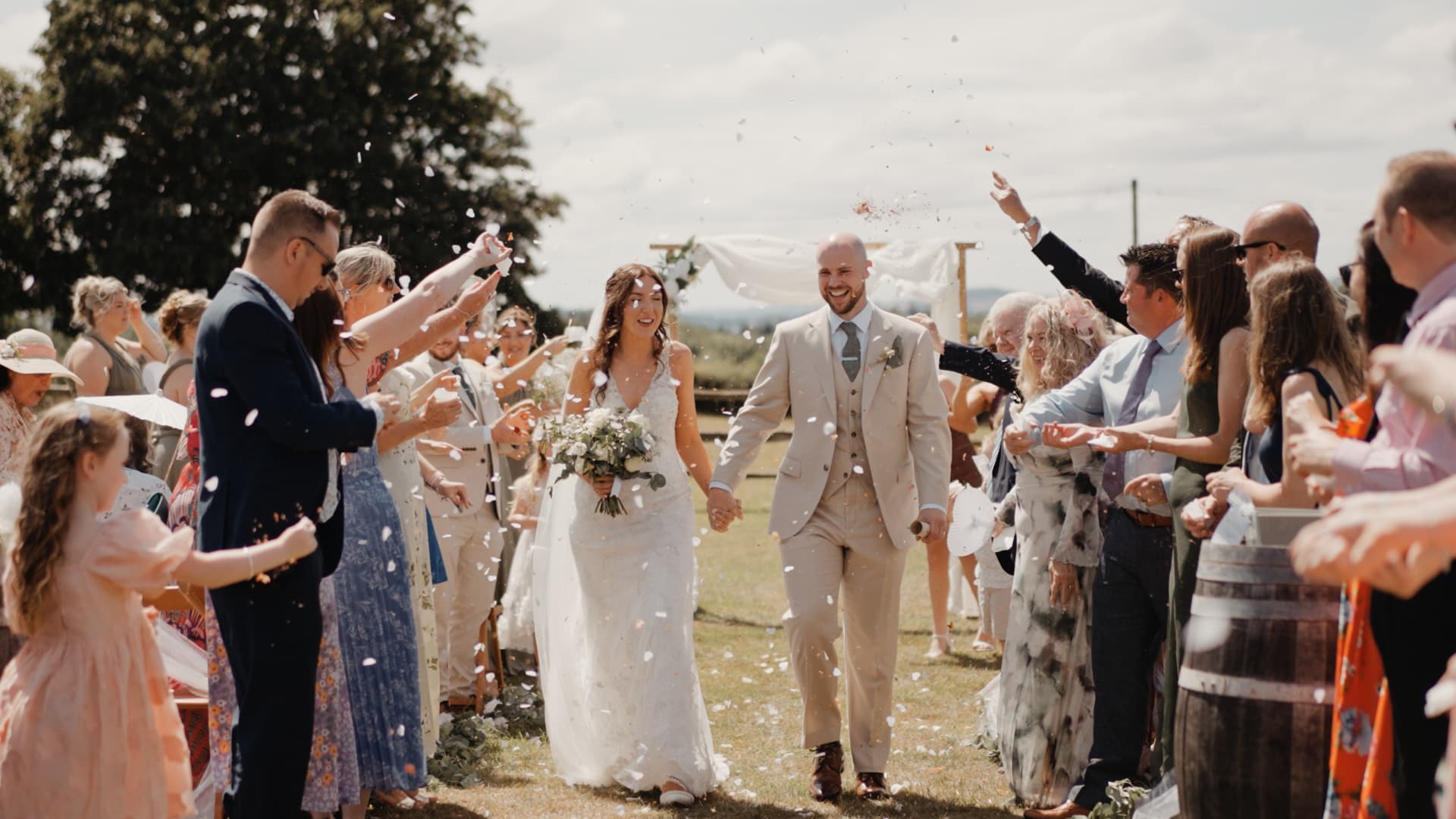 Bride and groom walking through guests during their confetti exit at Humber Barn, smiling as petals fill the air on a sunny summer afternoon.