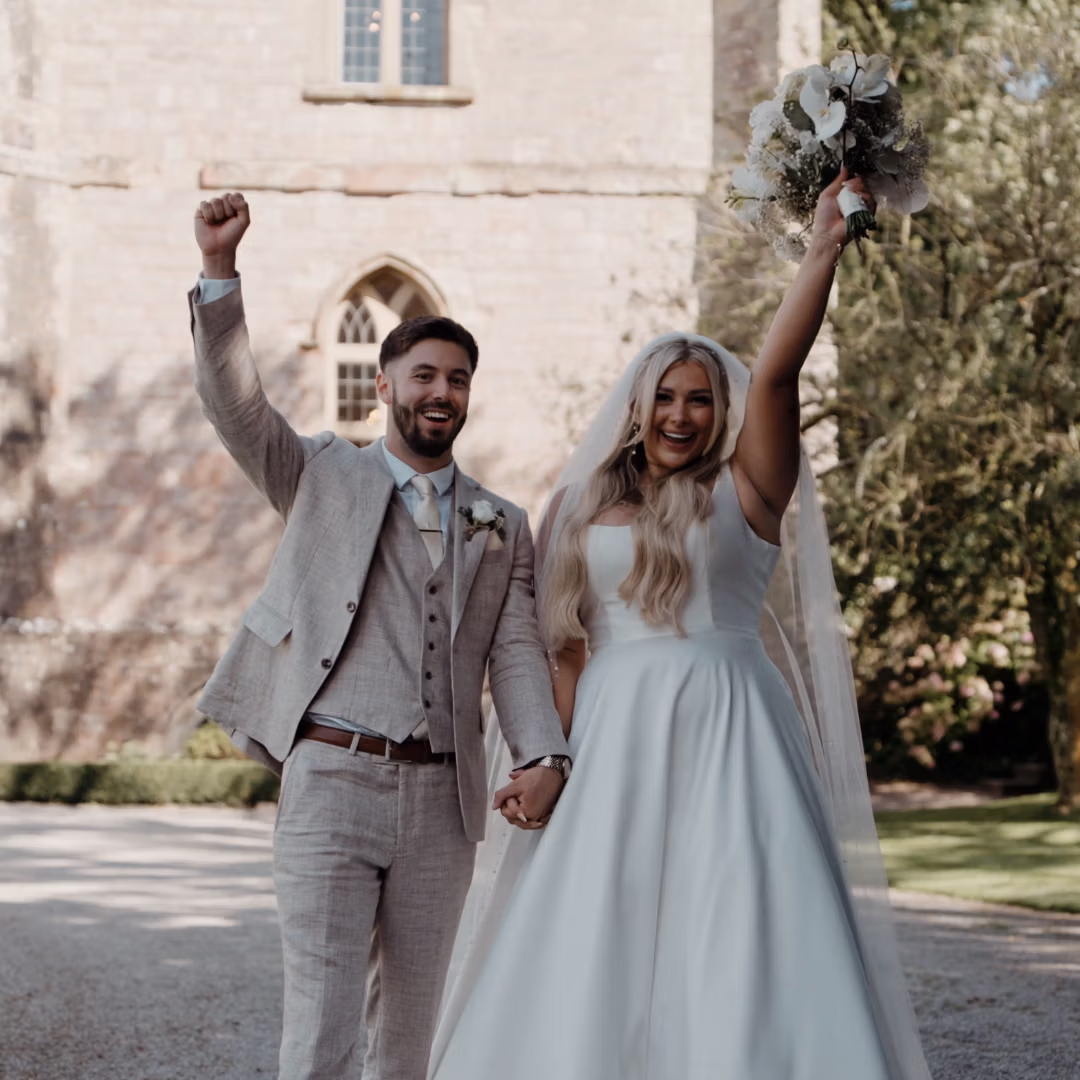 Bride and groom walking along with her bouquet and his hand up in the air.