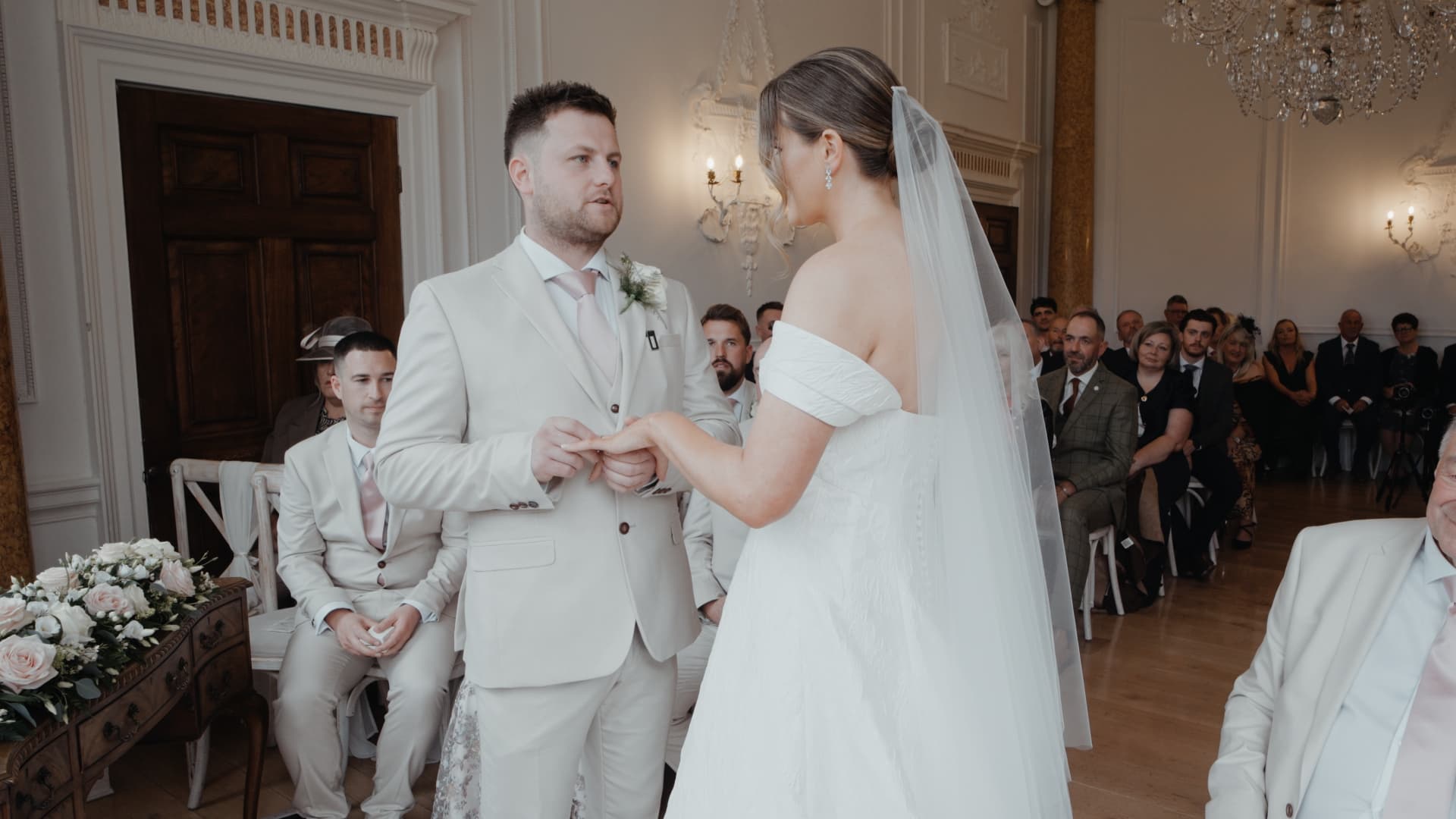 Bride and groom exchange wedding rings during an intimate ceremony at Rockbeare Manor, surrounded by family and friends.