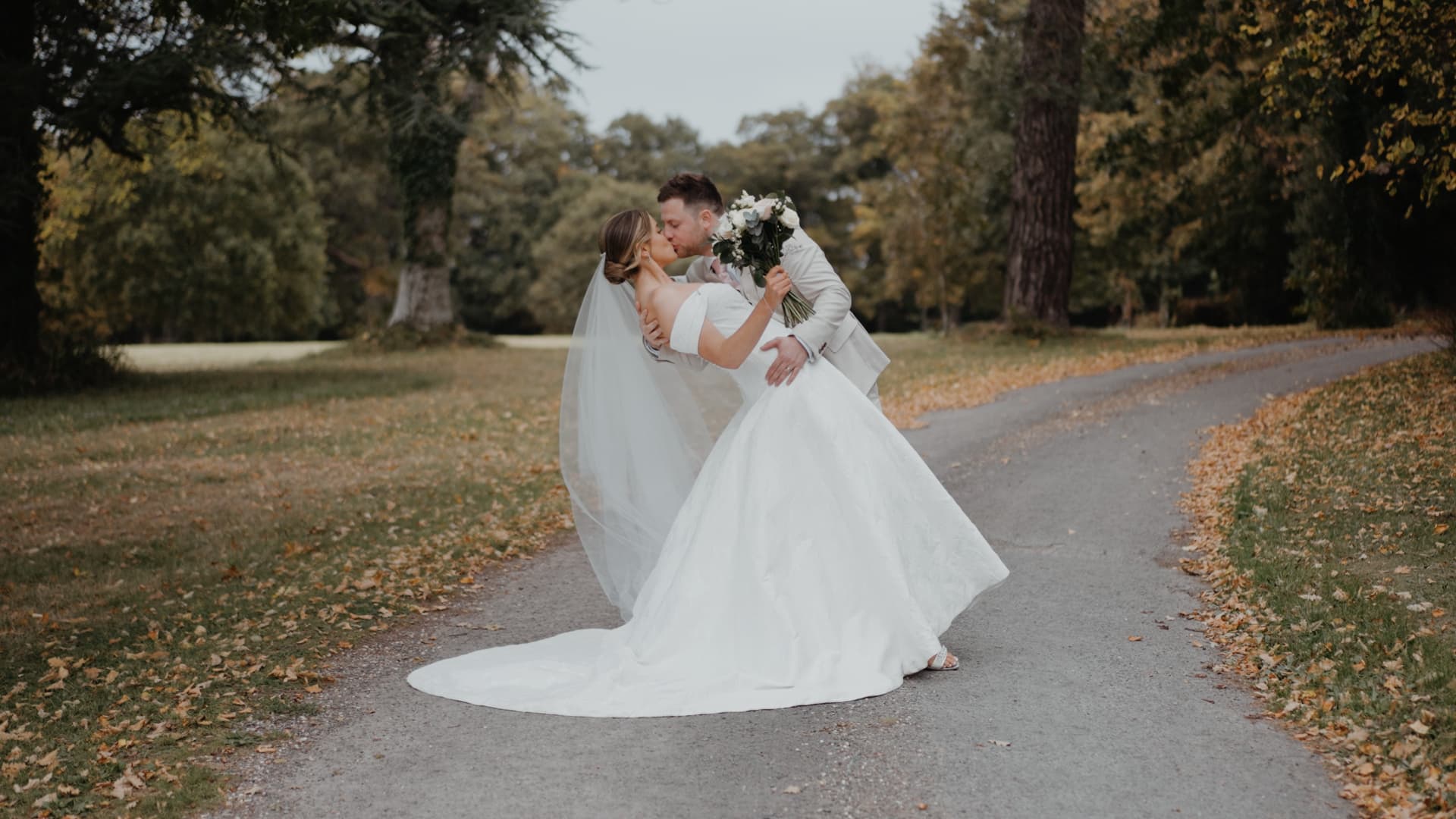 Bride and groom share a romantic dip kiss surrounded by autumn leaves at Rockbeare Manor in Devon.