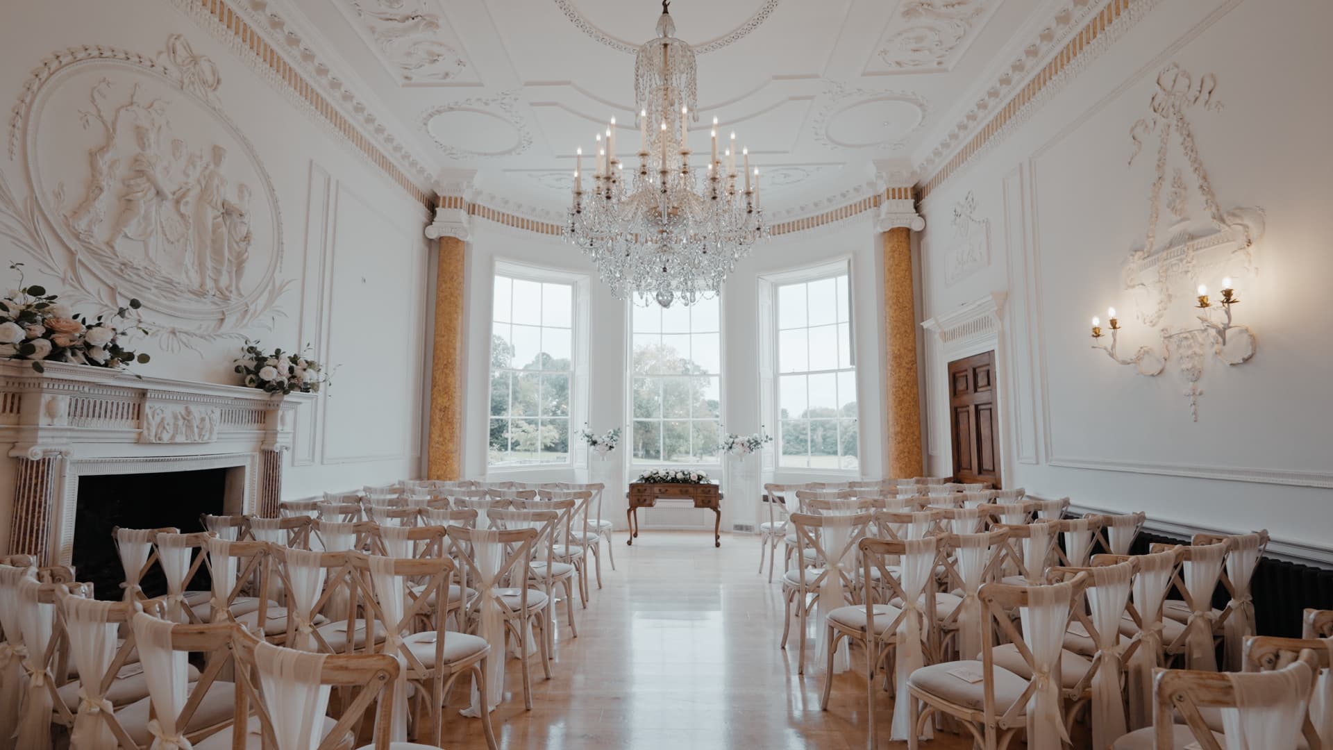 The ceremony room at Rockbeare Manor featuring a grand chandelier, Georgian architecture, and elegant floral decor.