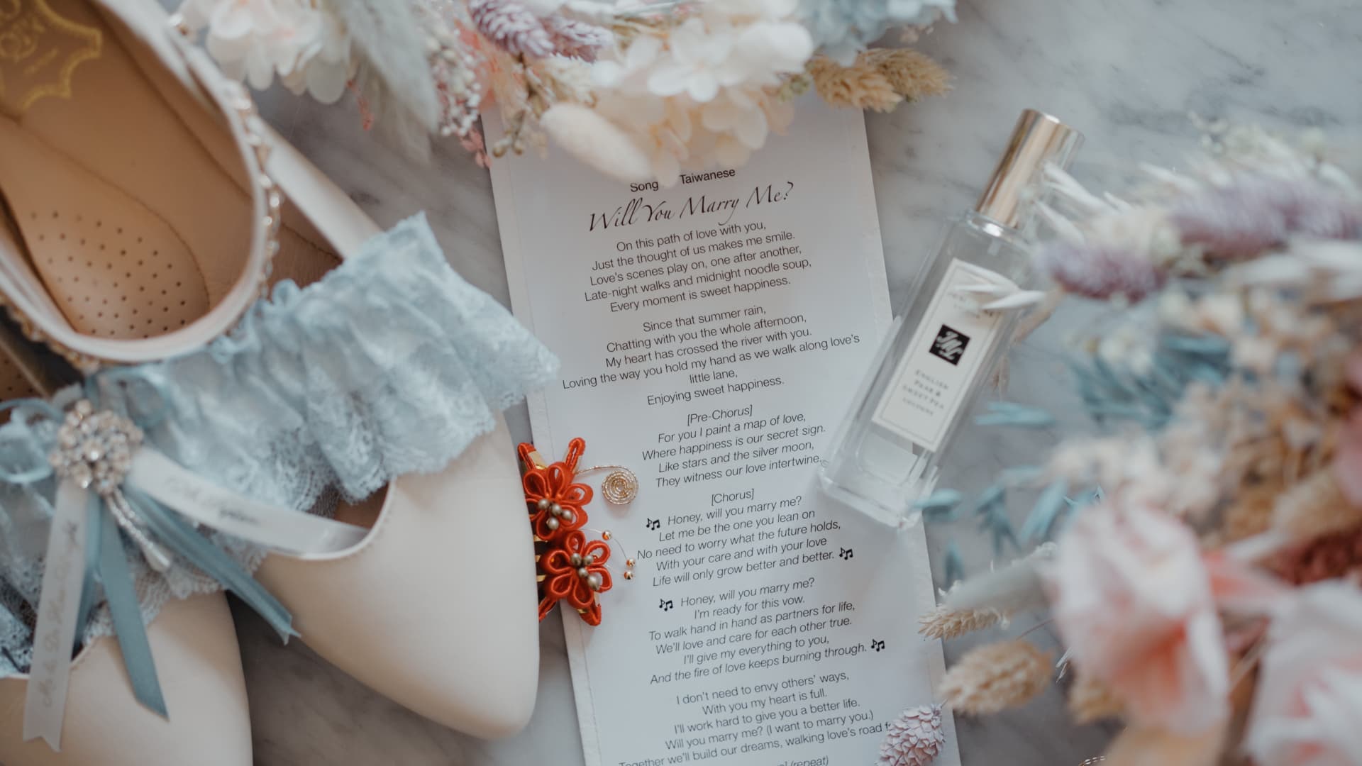 Flatlay of meaningful wedding morning details including shoes, a lace garter, a Taiwanese song sheet and florals, captured for their fusion wedding story.