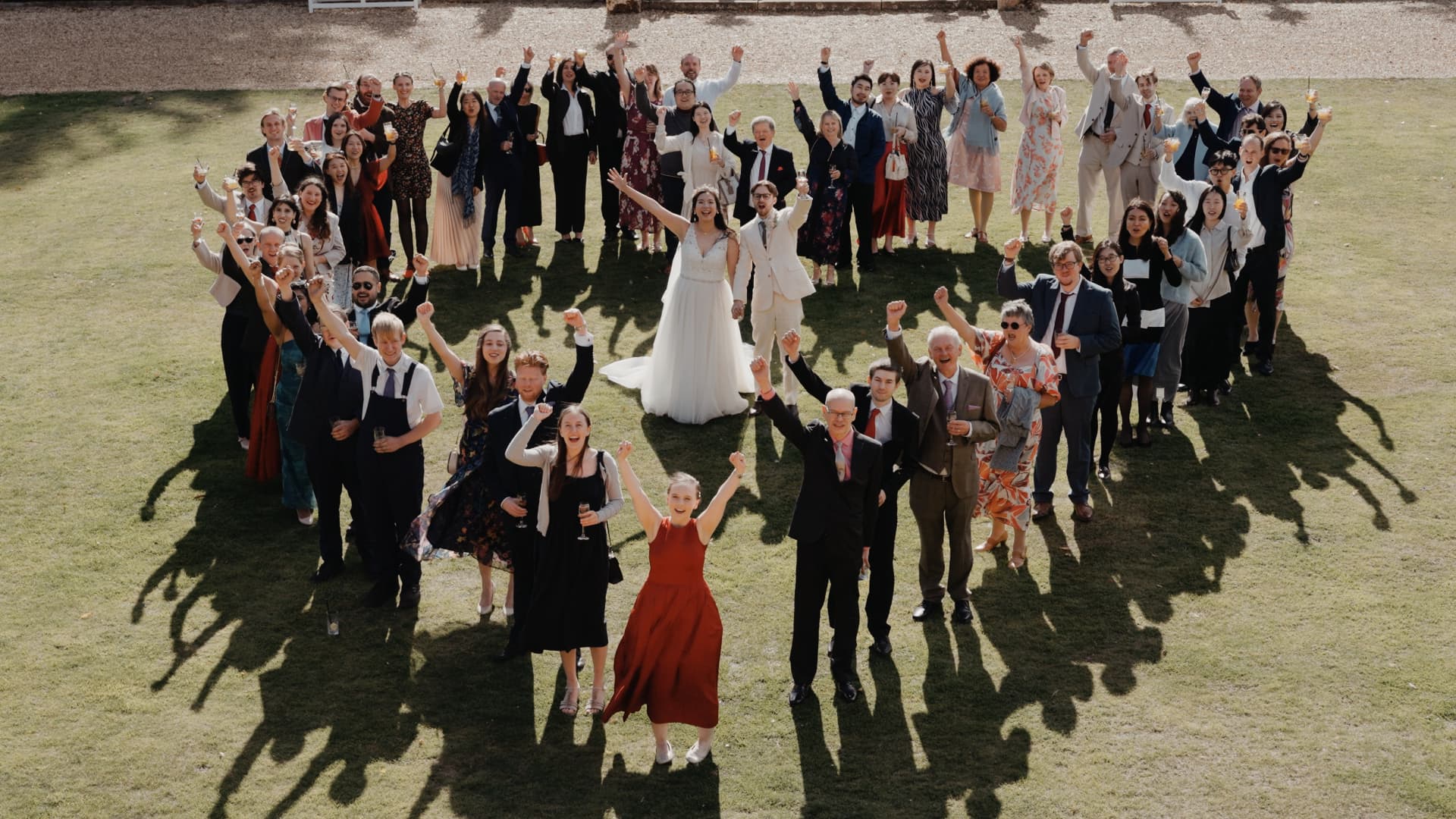 A joyful group photo on the lawn as guests cheer and gather around the couple during their fusion wedding.
