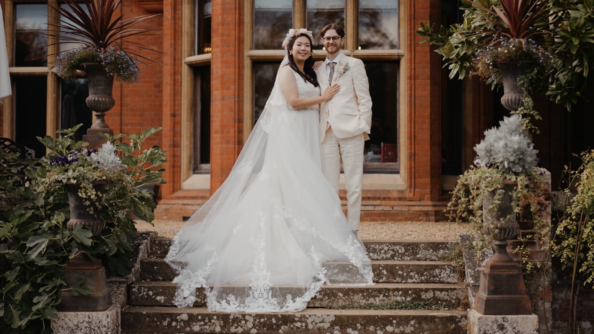 Wan-Ting and James standing together on the stone steps of Holmewood Hall during their elegant wedding portrait session.