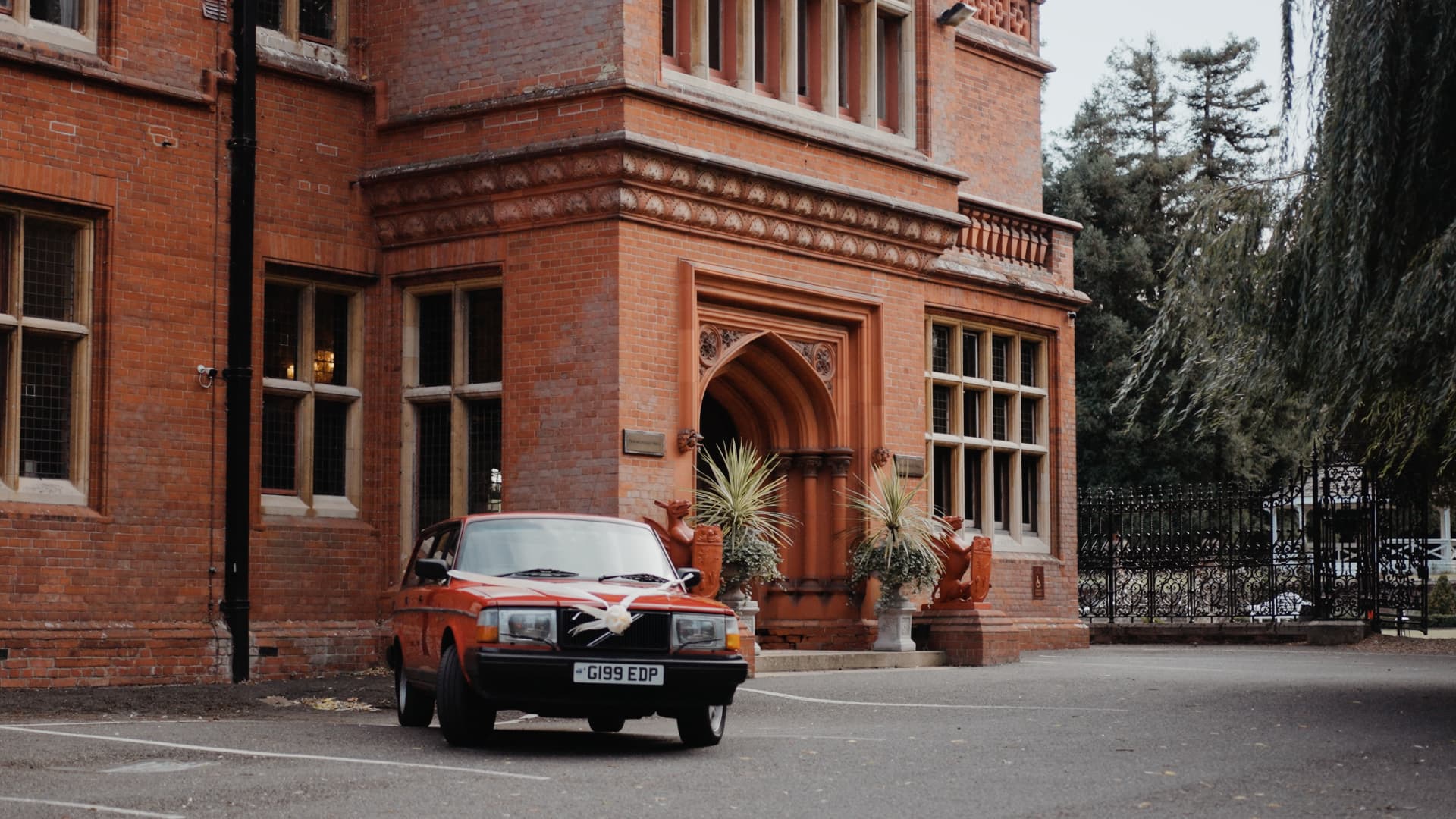 Vintage red wedding car parked outside Holmewood Hall’s grand red-brick exterior, adding charm and character to this fusion wedding celebration.