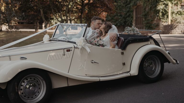 Bride and groom sharing a romantic kiss in their vintage car at a Cadbury House Wedding.