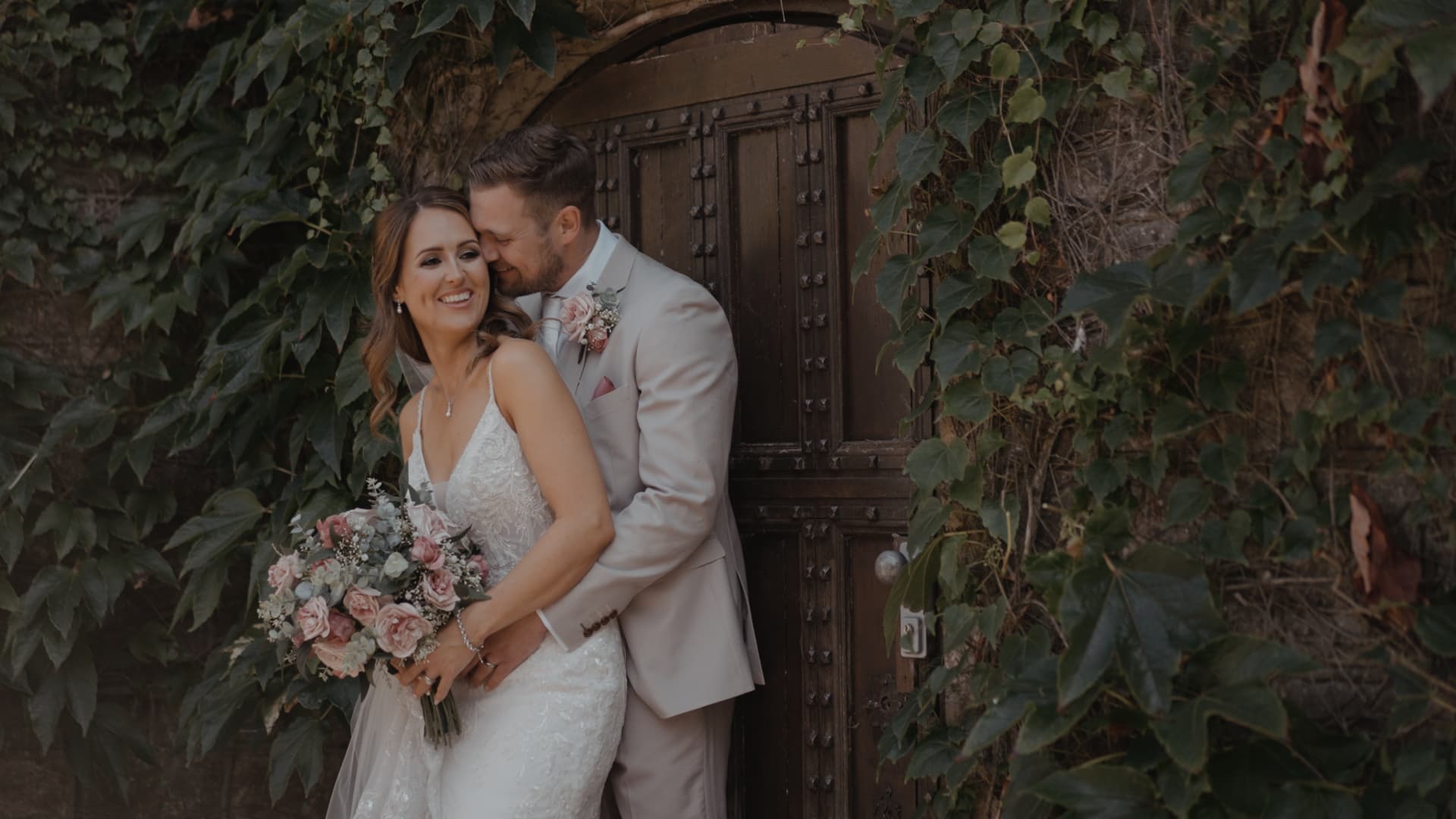 Bride and groom embracing by the ivy-covered doorway captured by their wedding videographer.