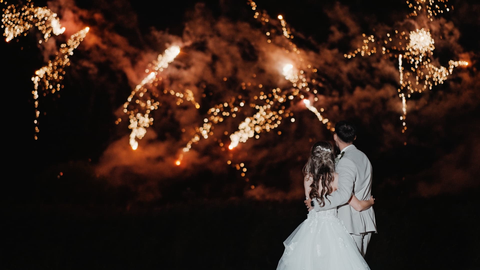 Bride and groom watching a golden fireworks display at night at Quantock Lakes Wedding Venue, captured in a romantic moment from their lakeside celebration.