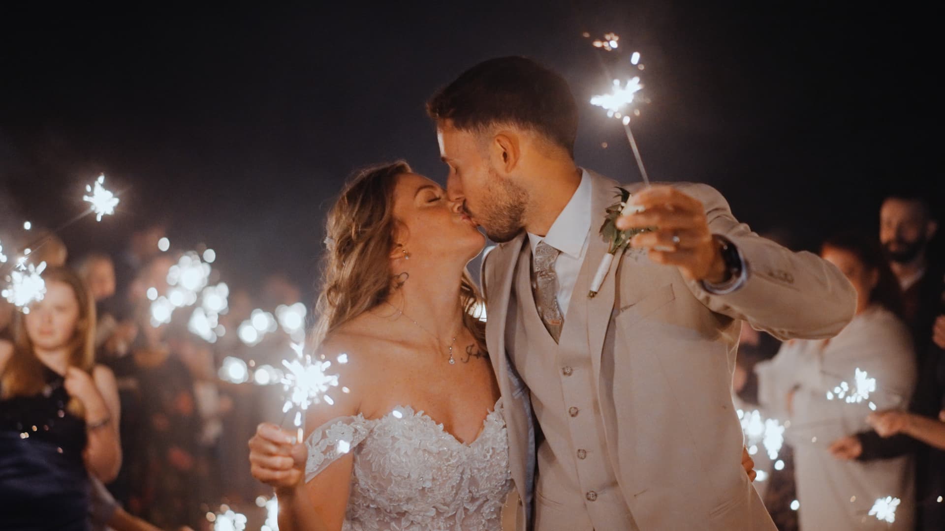 Bride and groom sharing a joyful sparkler kiss surrounded by guests during their evening celebration at Quantock Lakes Wedding Venue.