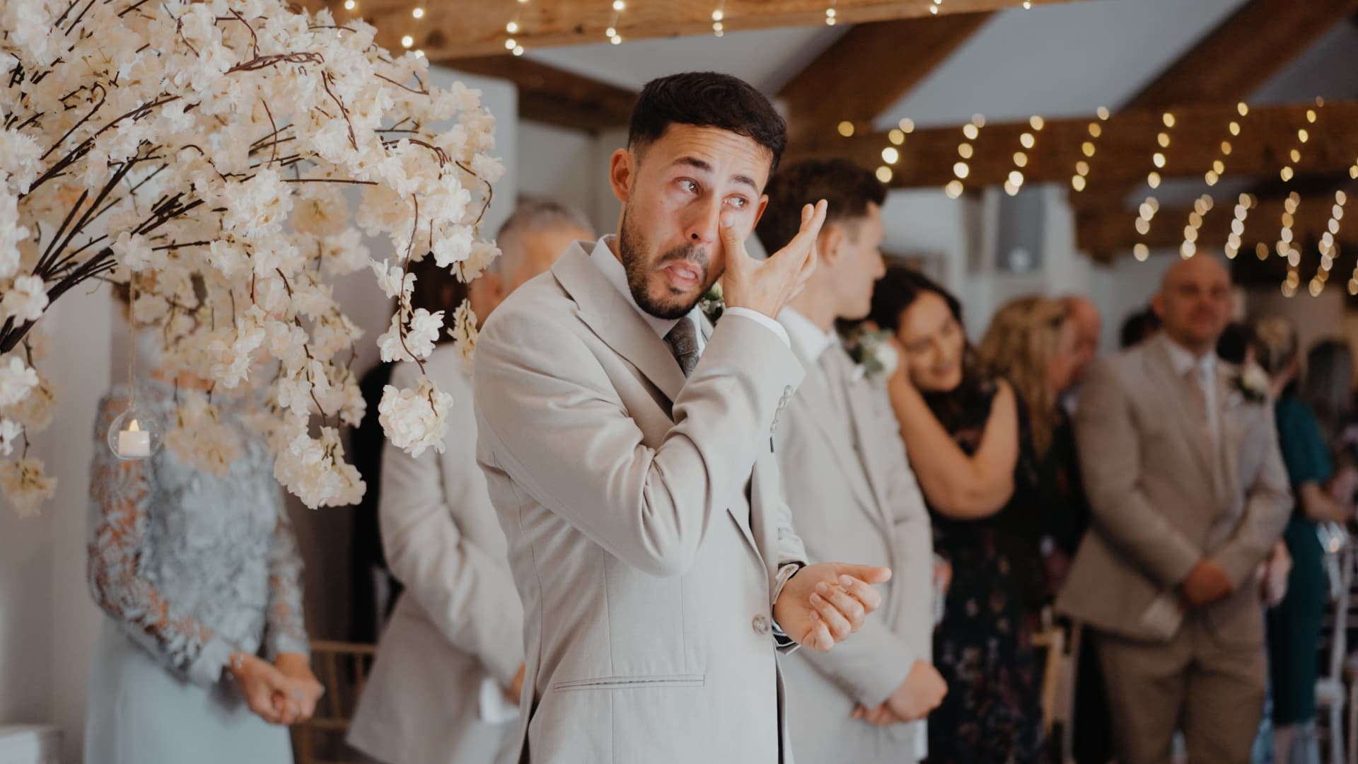 Emotional groom wiping tears during the ceremony under soft floral décor and fairy lights at Quantock Lakes Wedding Venue.