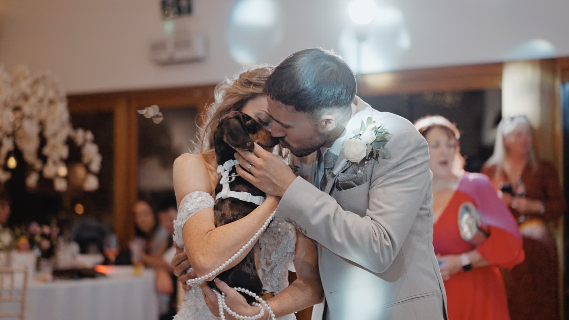 Bride and groom sharing a sweet moment as they kiss their dachshund during their rustic countryside wedding celebration.