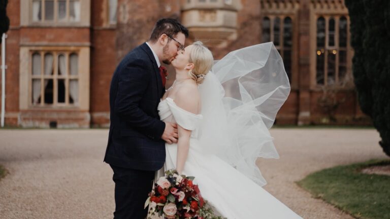 Romantic couple kiss portrait during a St Audries Park wedding with flowing veil and burgundy bouquet in front of the manor house