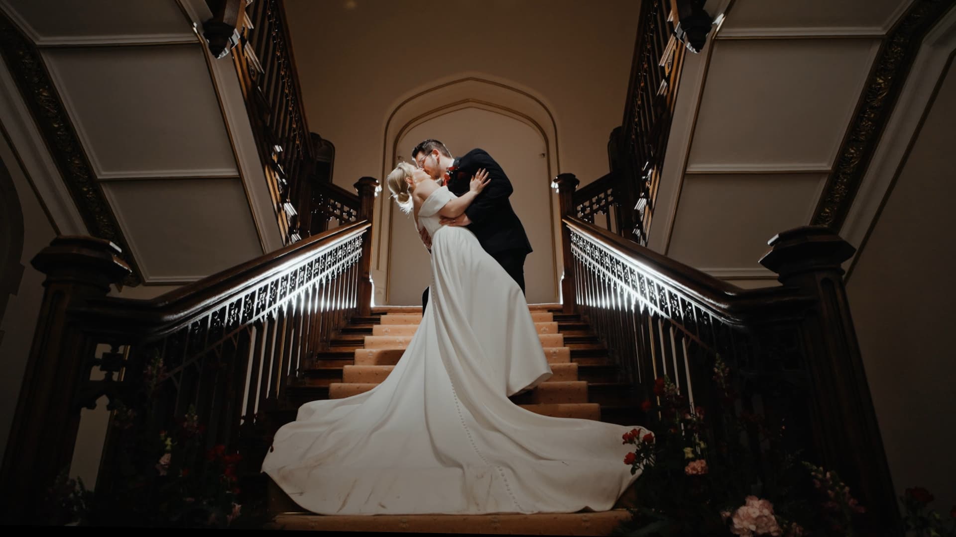 Cinematic staircase kiss at St Audries Park wedding captured as a luxury wedding film with dramatic lighting and elegant bridal gown