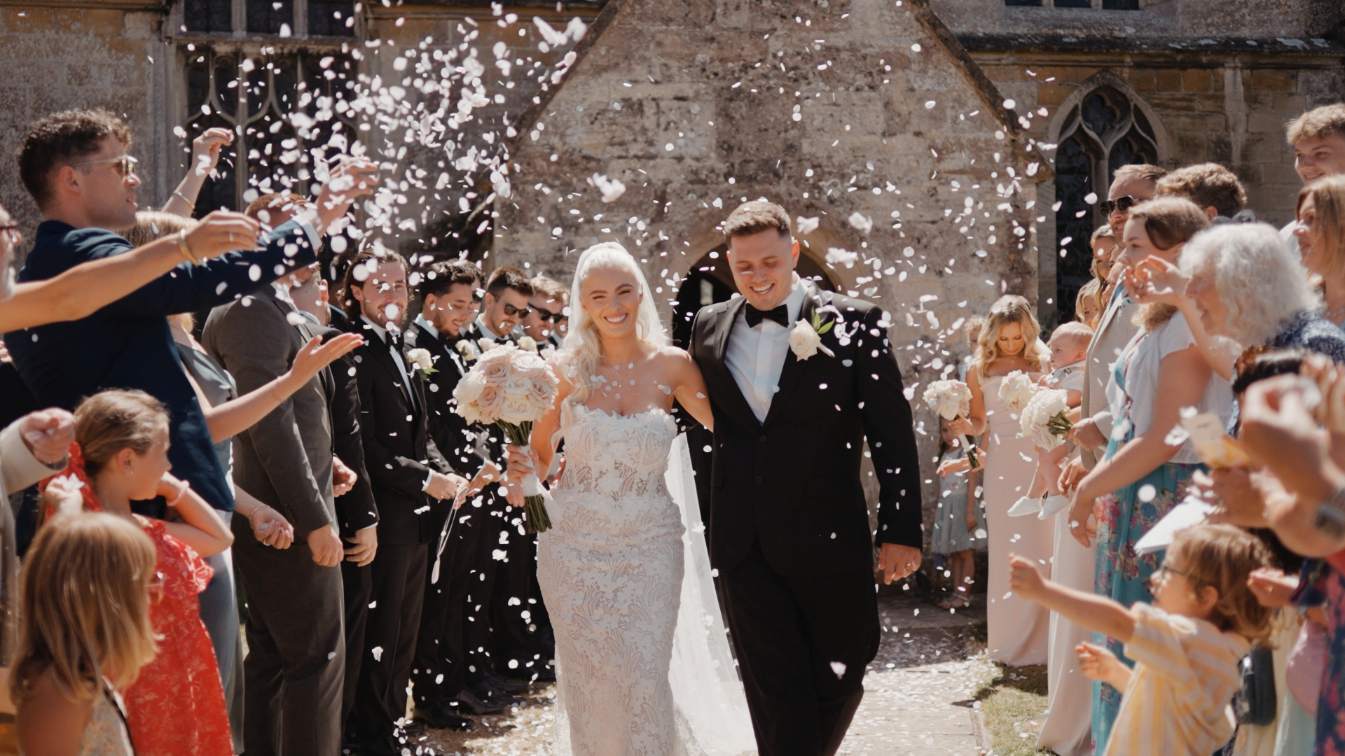 Bride and groom walking through confetti outside Eastington Park in Gloucestershire, a joyful client love moment captured by a Somerset wedding videographer