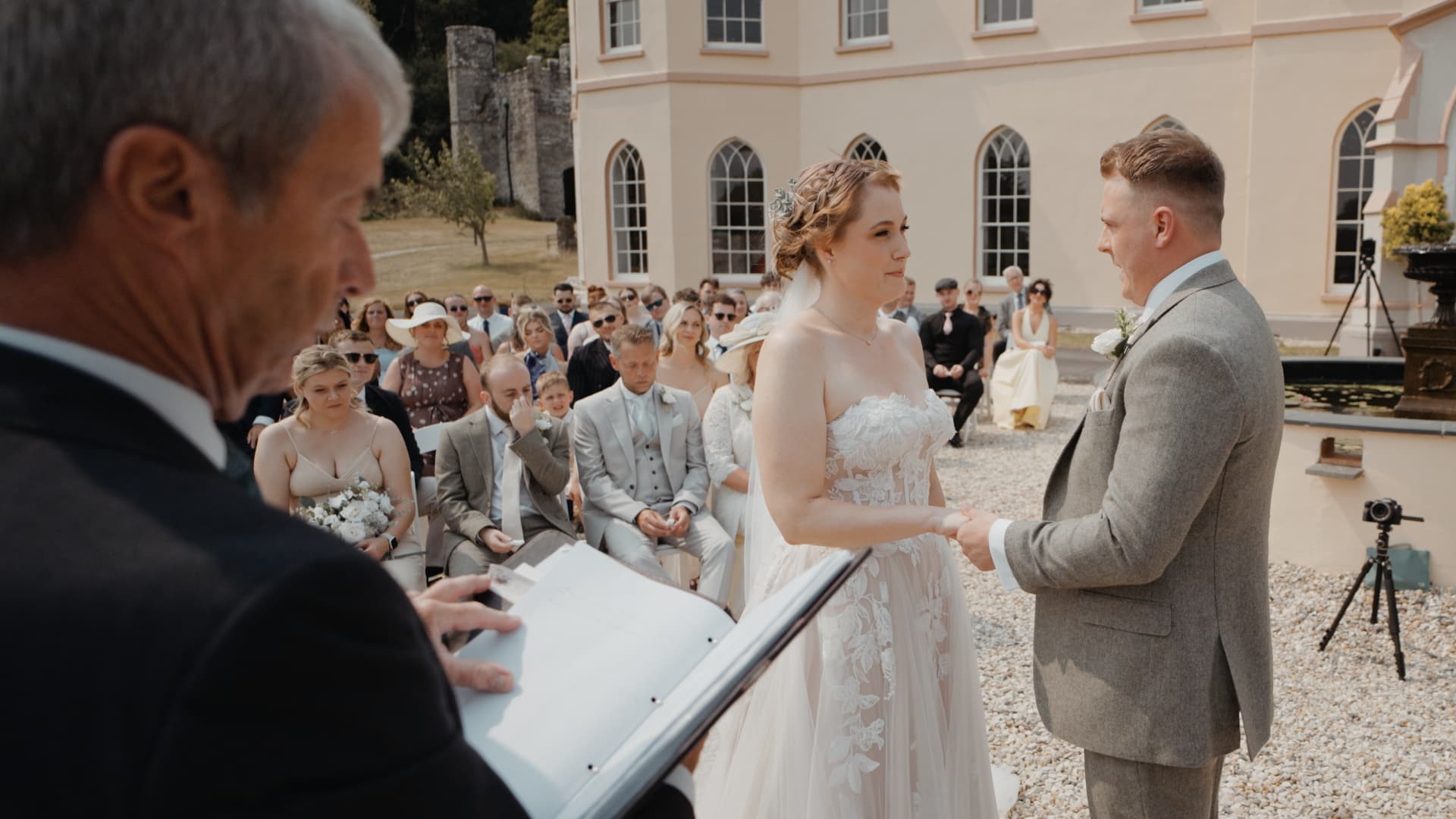 Bride and groom holding hands during their ceremony at Tawstock Court, a Devon wedding venue, filmed by a Devon wedding videographer in a natural documentary style