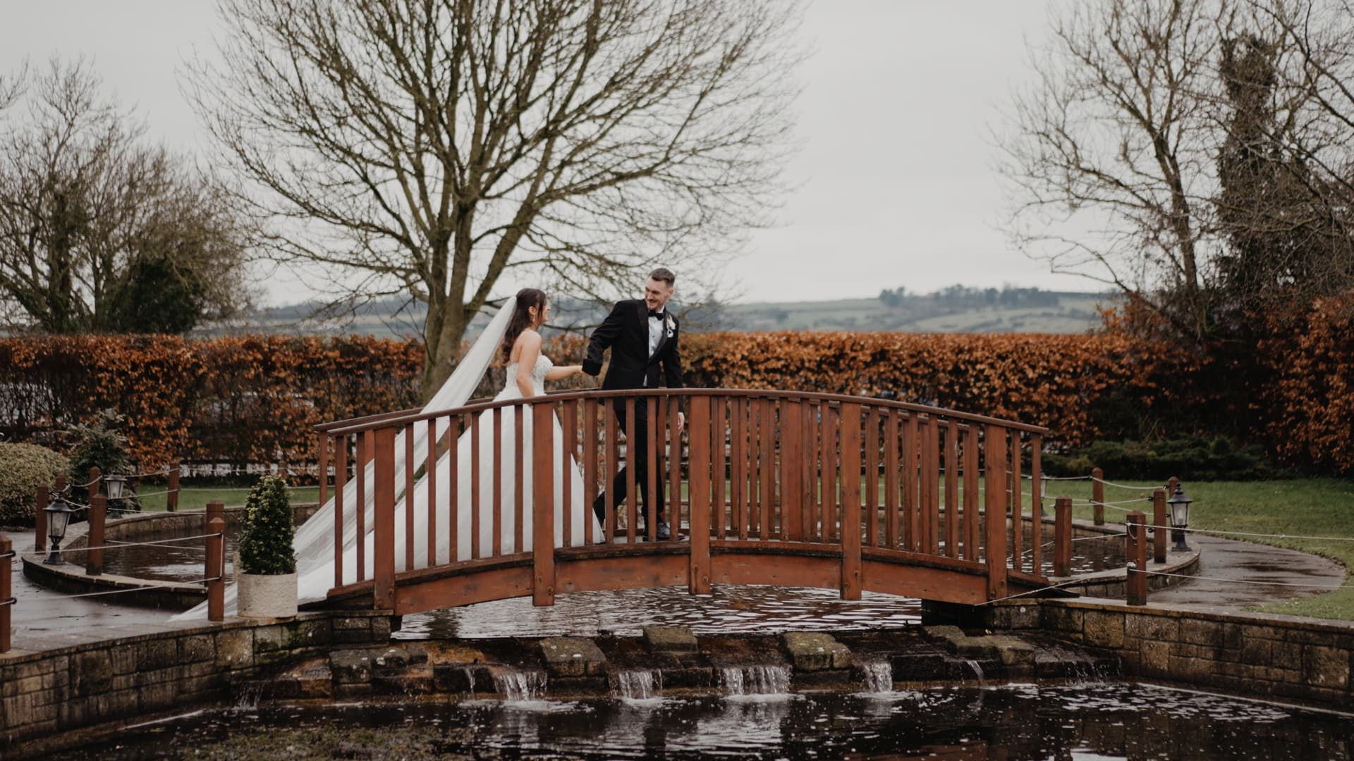 Bride and groom walking across a wooden bridge at Batch Country House in Somerset, captured naturally in luxury documentary wedding videography by a Somerset & South West wedding videographer