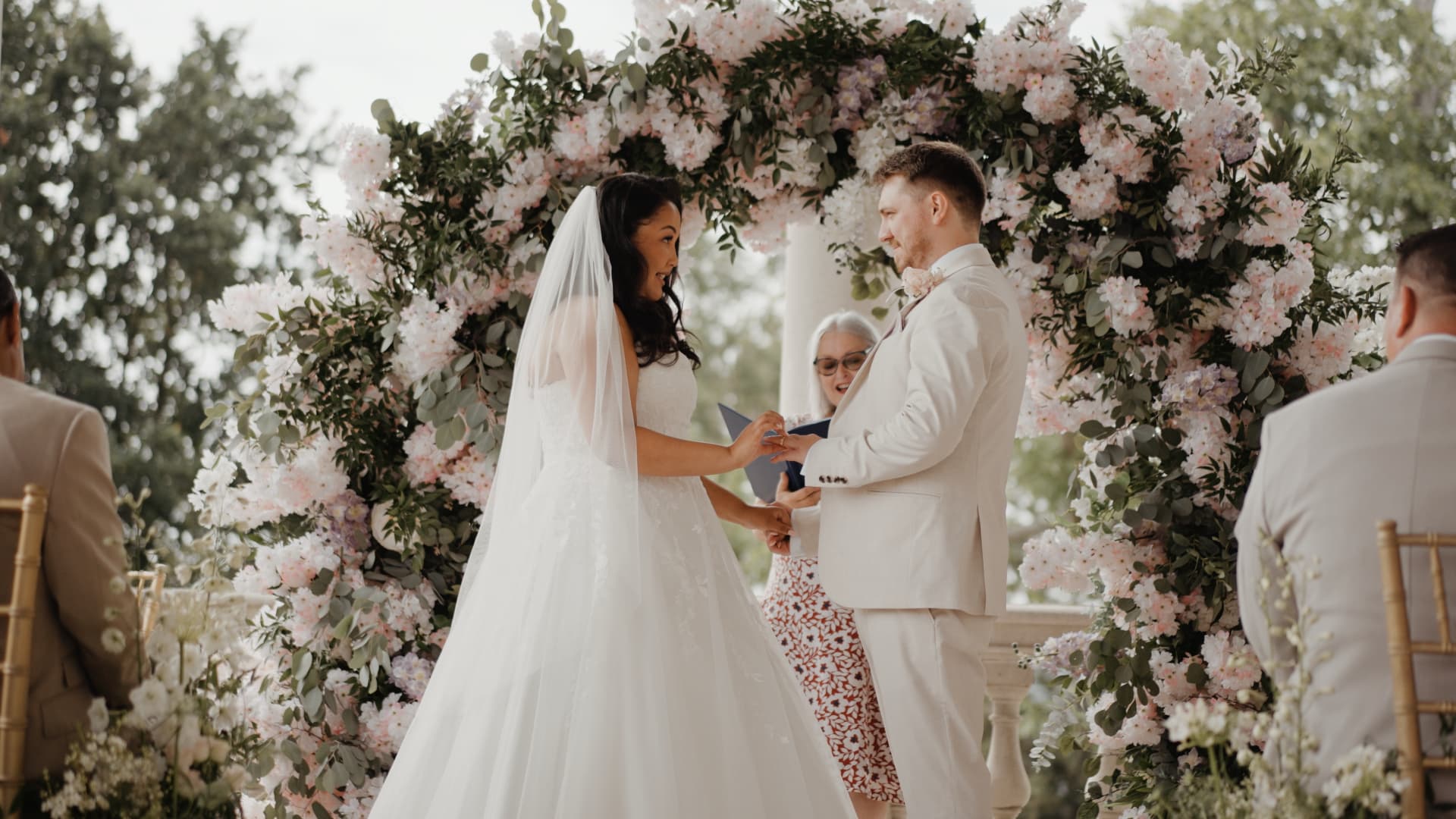 Bride and groom exchanging rings beneath a floral arch during an outdoor ceremony at Cliveden House, captured in a luxury wedding film by a wedding filmmaker